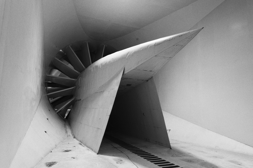 A large wind tunnel fan with angled blades is positioned in a smooth-walled chamber.