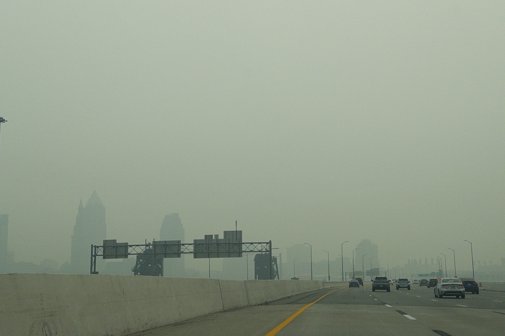 A highway stretching toward a city skyline obscured by heavy smog or fog with several vehicles on the road.