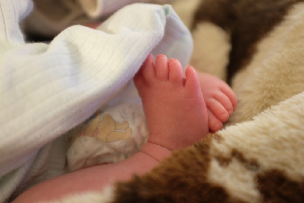 A newborn baby's tiny feet peek out from under a soft blanket.