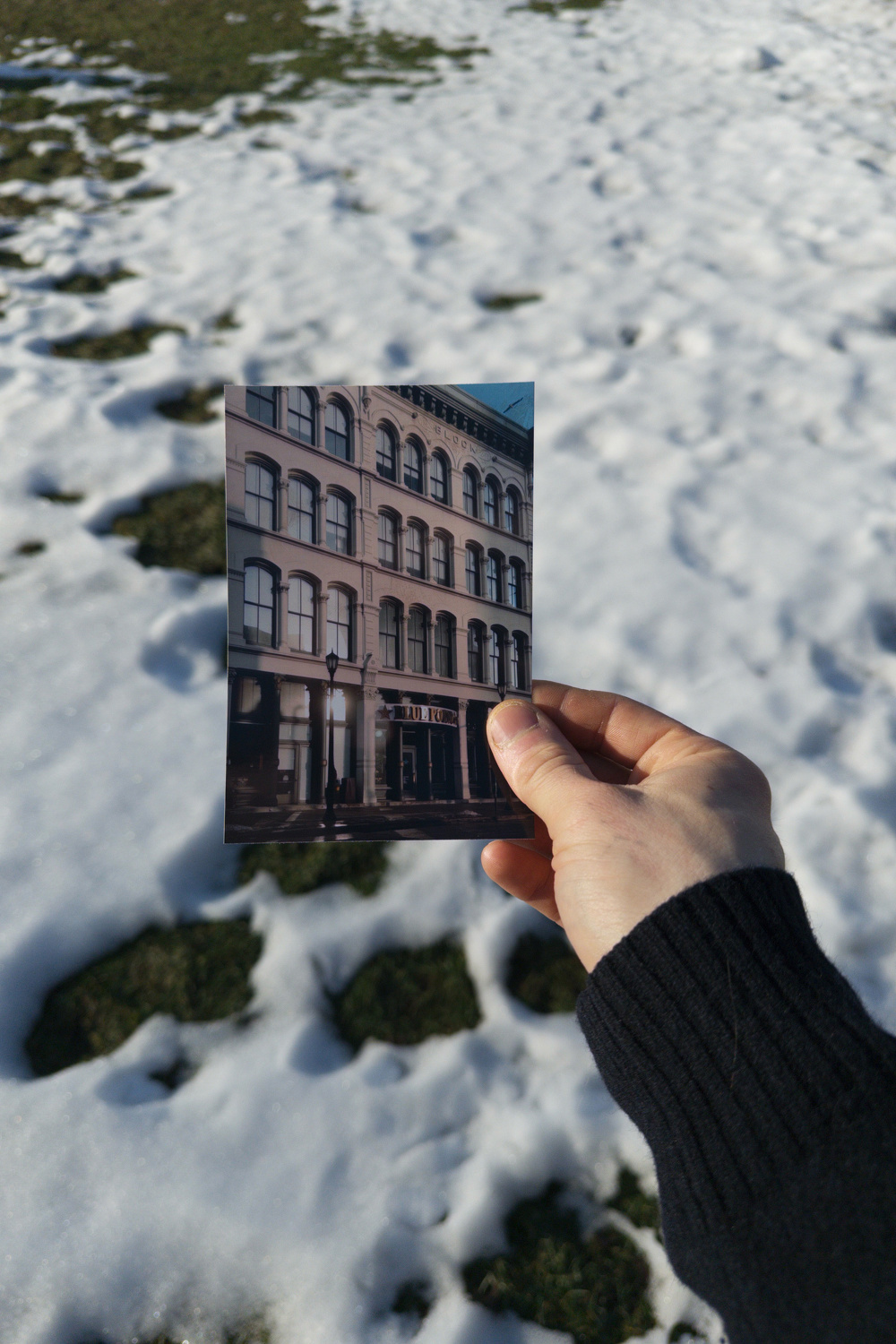 A hand is holding a photo of a building against a snowy ground backdrop.