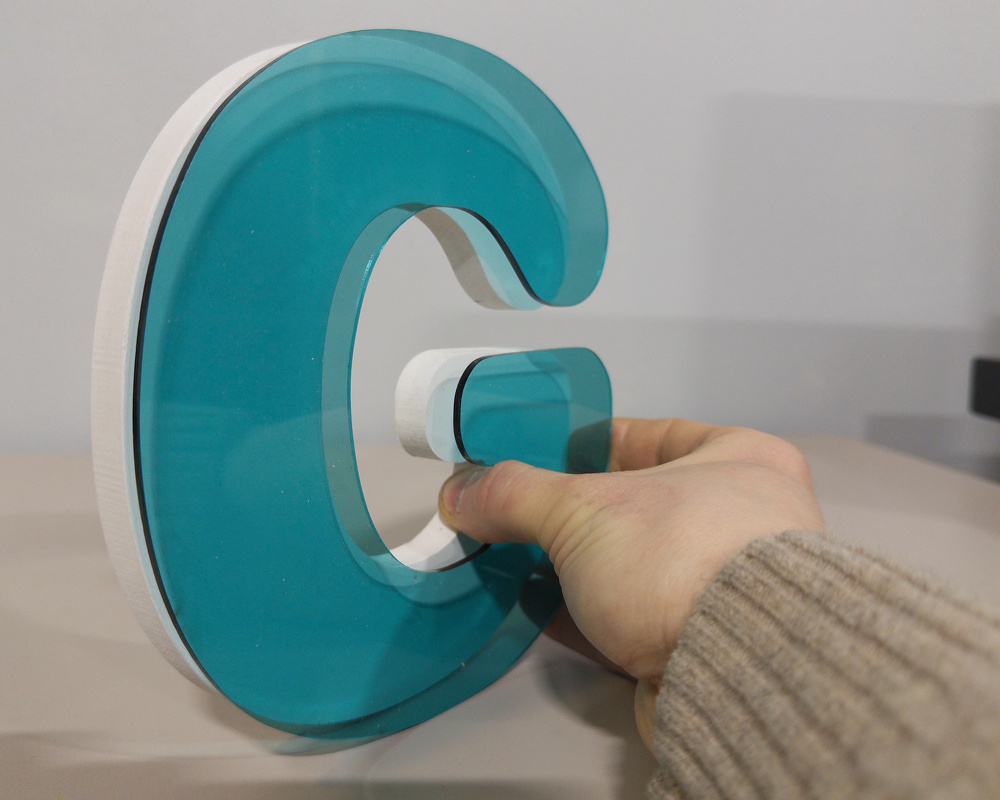 A hand is holding a large, translucent turquoise letter G.