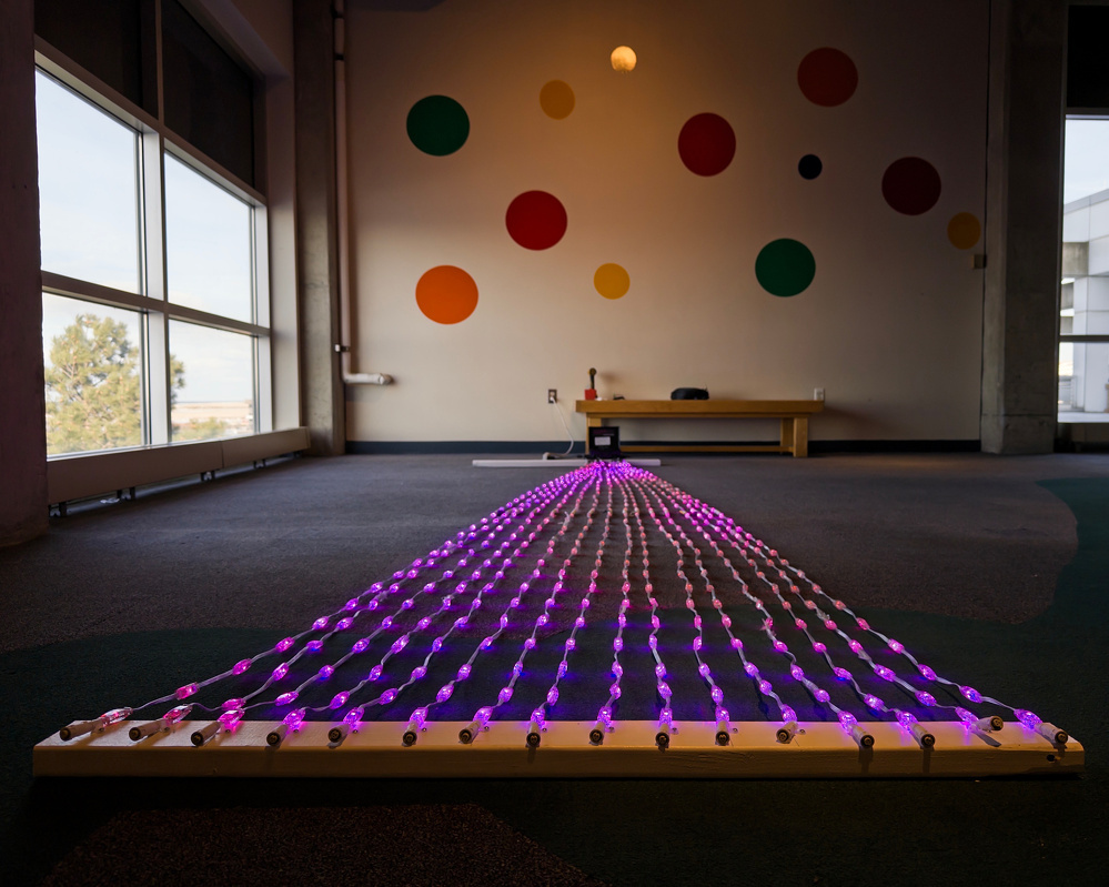 A pathway of purple LED lights is displayed on a floor next to a wall decorated with colorful circles.