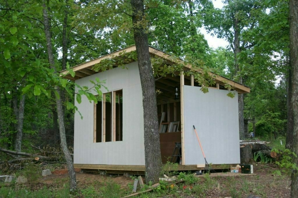 Partially built tiny house in the woods. Missing front windows and door.