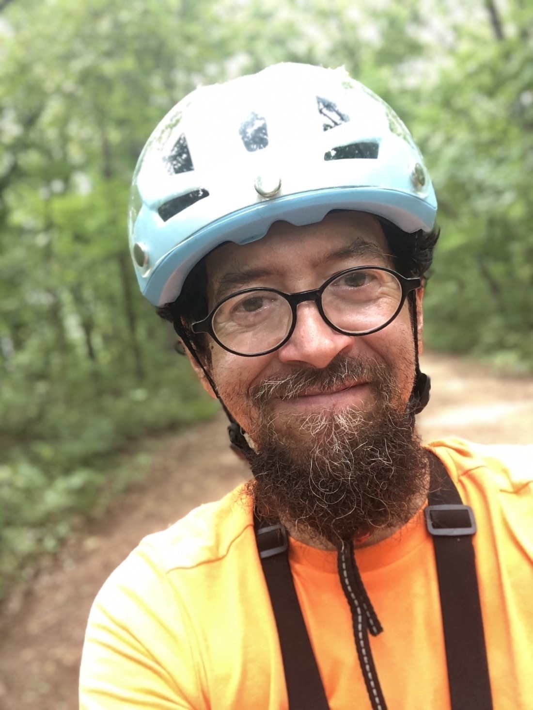 A beardy guy with glasses wearing a bluy cycling helmet and orange jersey