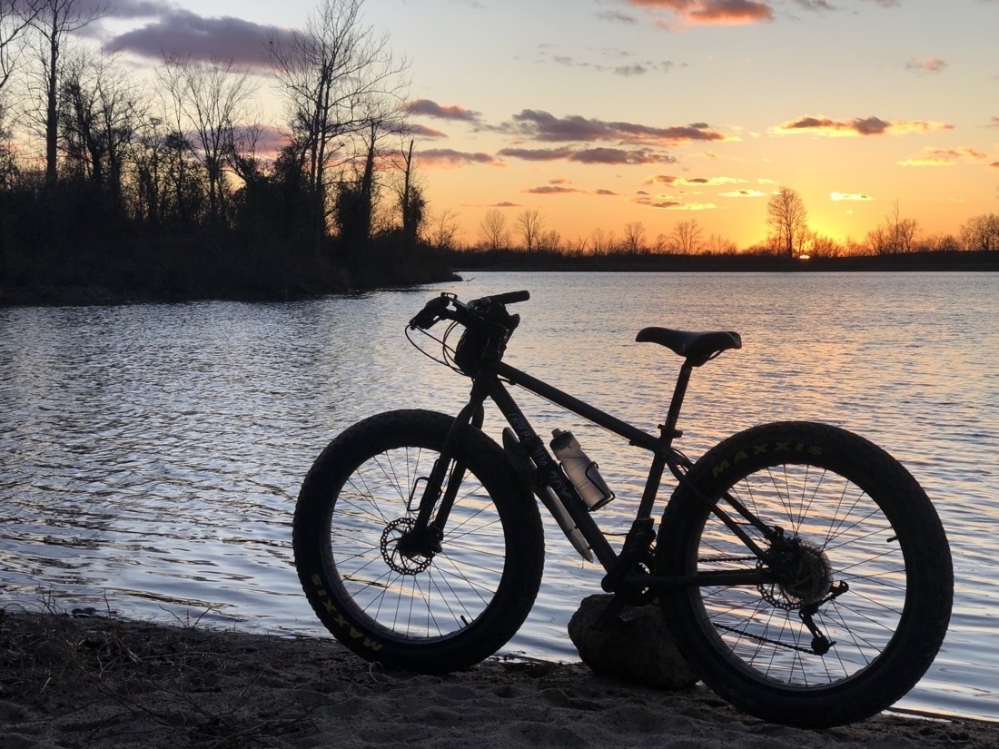A fat bike parked near a lake at sunset