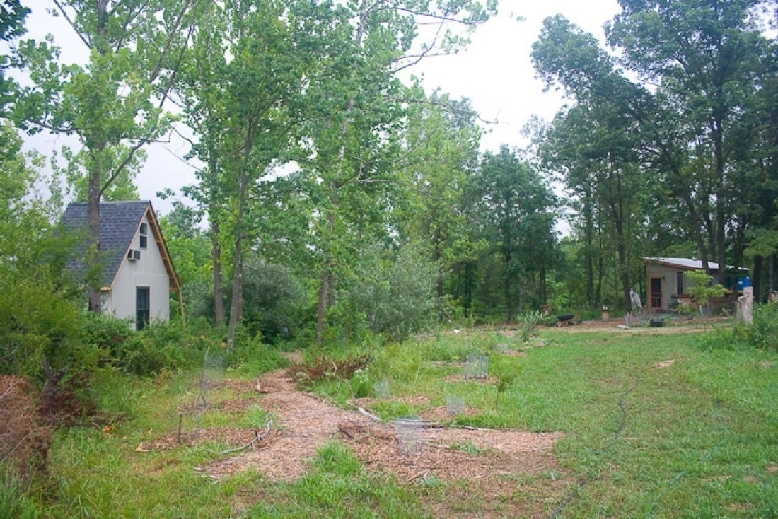 Various mulched paths with grass on the right side, two tiny house buildings in the background