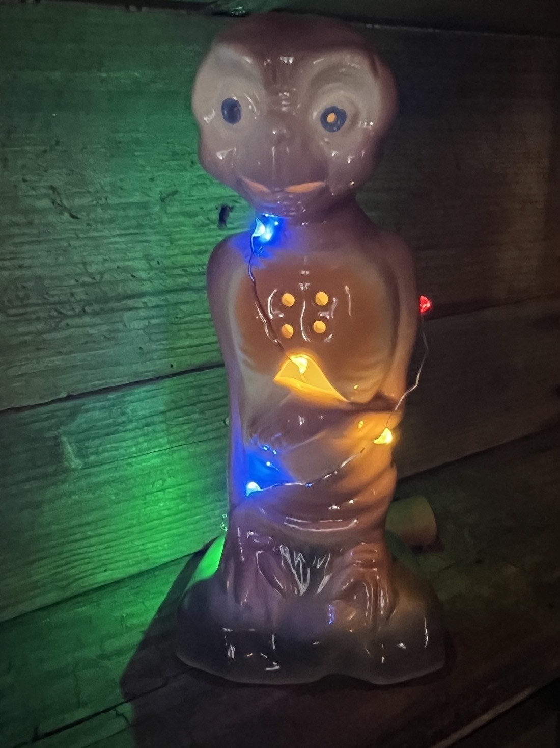 A ceramic E.T. Figurine, sitting on a shelf, decorated with colorful lights,