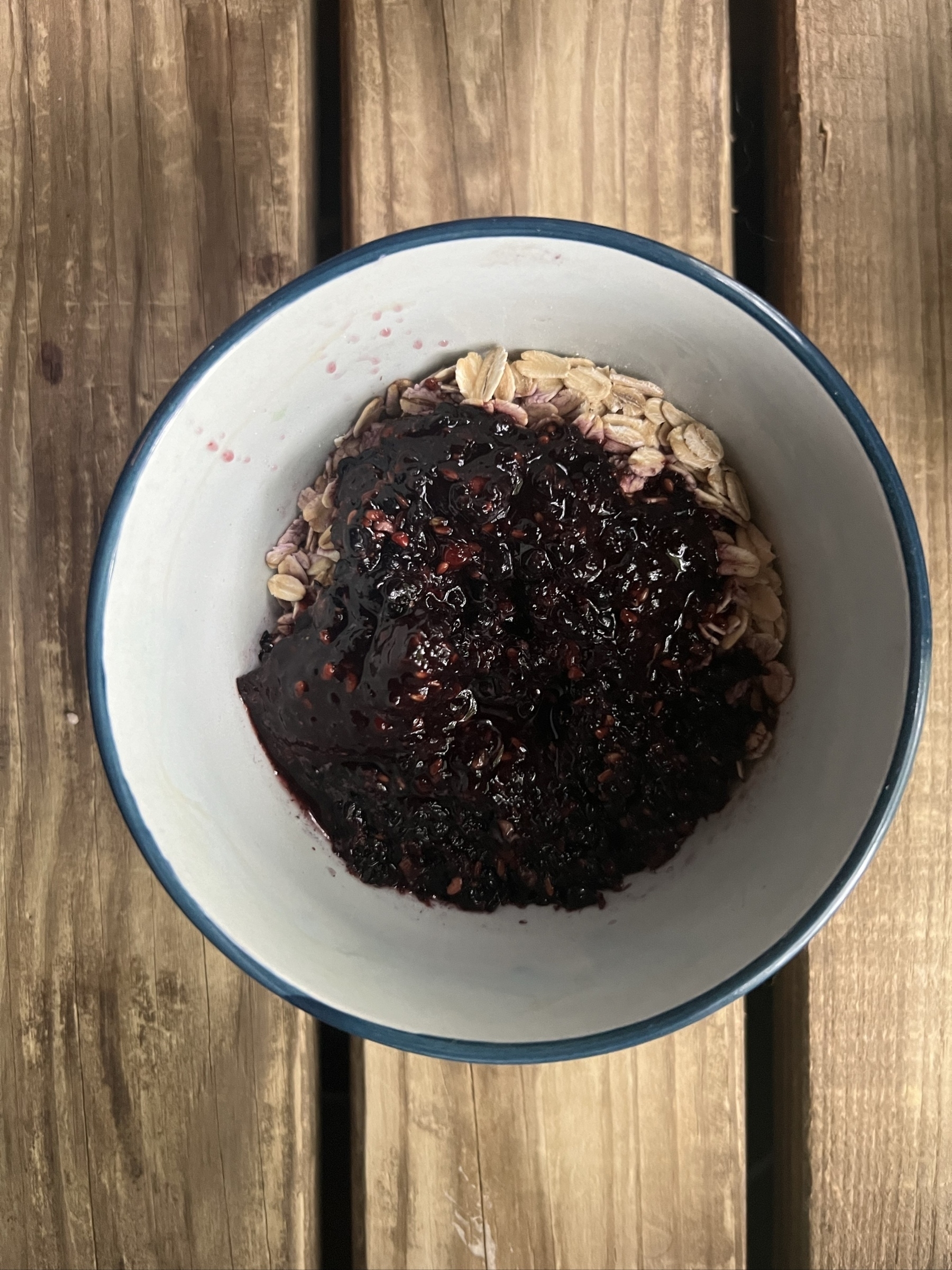 A bowl of uncooked oatmeal with a black-purple sauce of blended blackberries poured on top