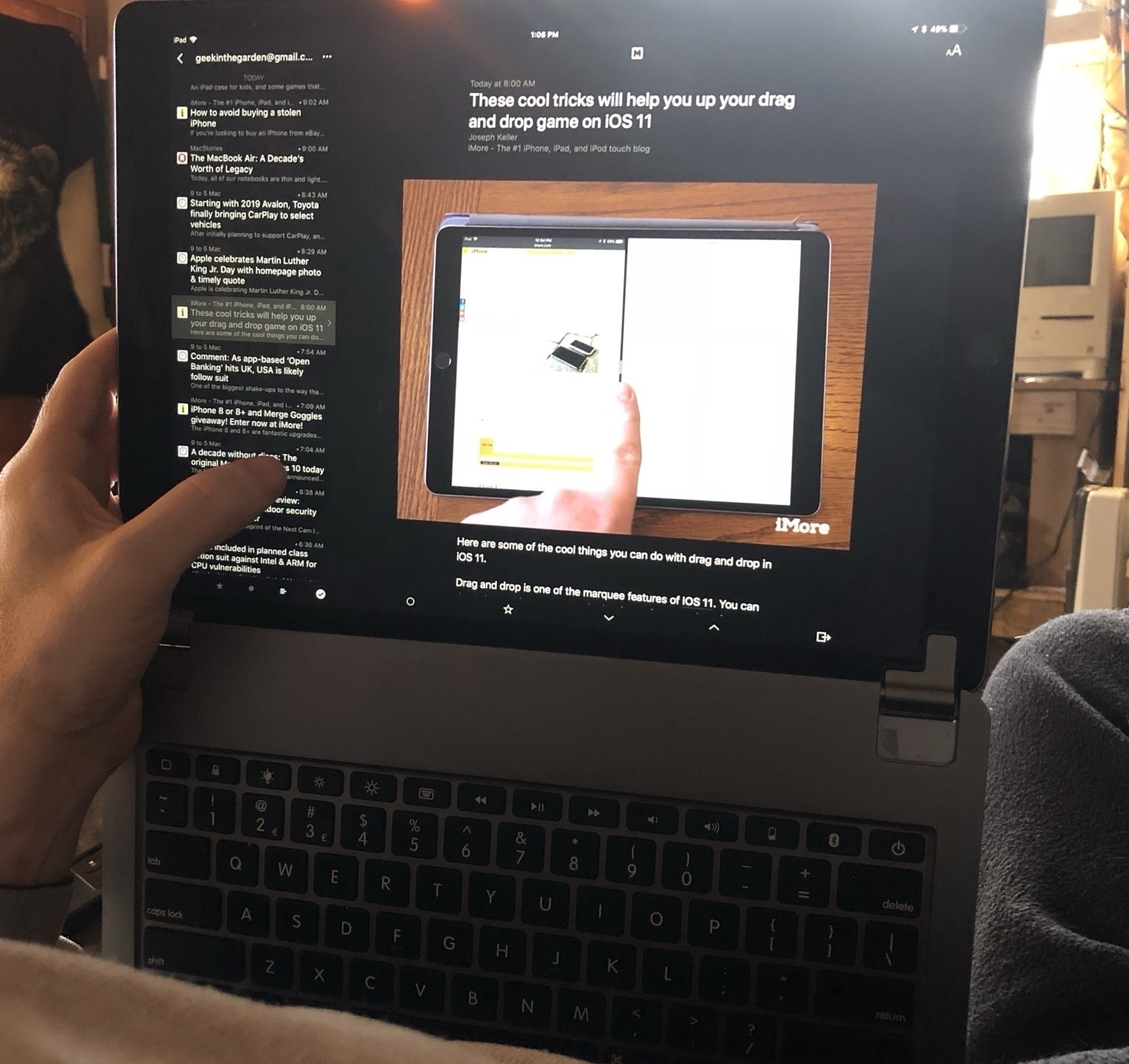 An iPad Pro being used with an aluminum Brydge keyboard. The iPad is oriented flat to the Brydge keyboard and being held vertically straight up such that the keyboard is serving to elevate the iPad off of a person's lap to eye level as they recline. A left hand is seen balancing the iPad. The screen displays the Reeder app for RSS.