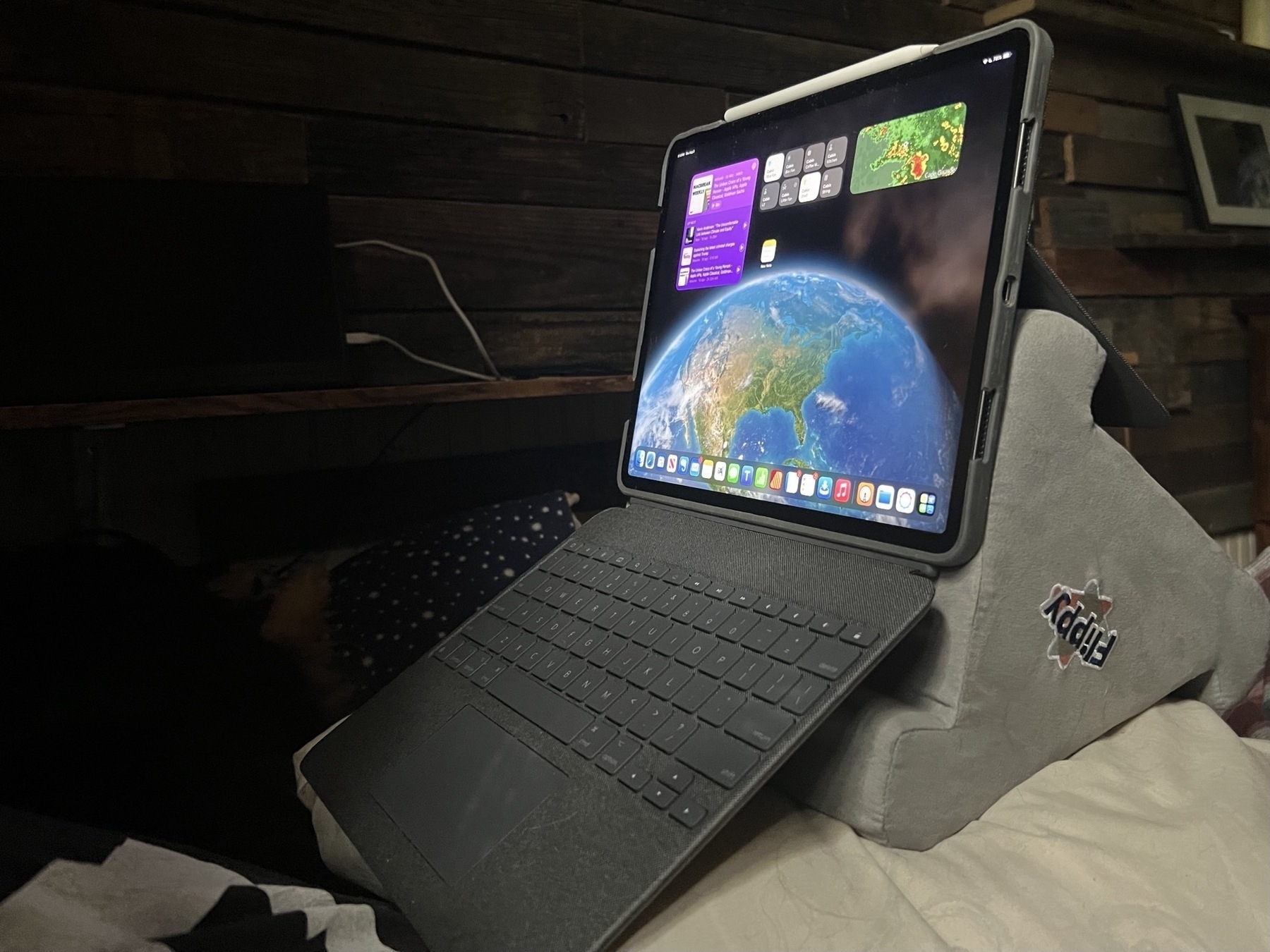 An iPad Pro in a Logitech Combo Touch keyboard for iPad is propped up over a tri-angle foam lap desk as a strange but effective angle for typing which holds the iPad at eye level.