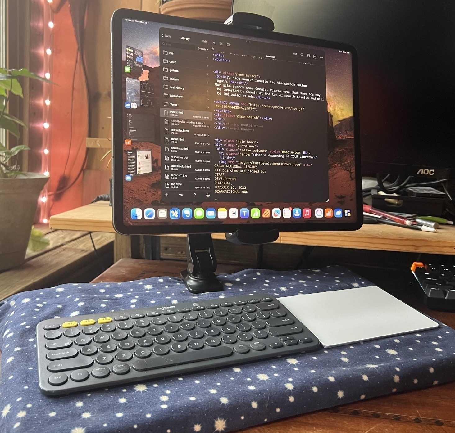 An iPad Pro floats above keyboard and trackpad on a lap desk. The iPad is held up by a configurable arm that is clamped to the back of the wood lap desk. Image taken is front of iPad so only the clamp is visible.