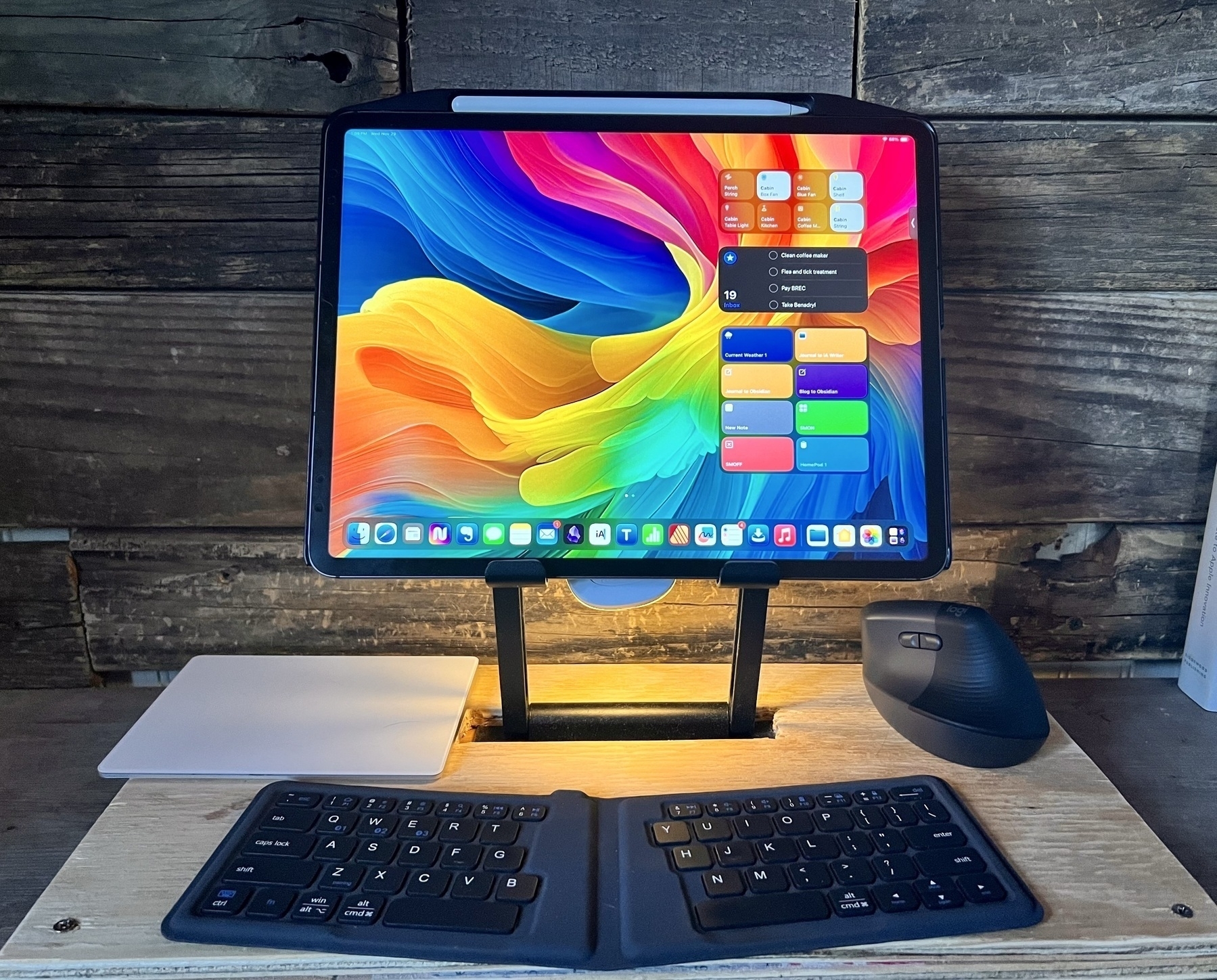 An iPad Pro on a stand that has been built into a plywood lap desk. In front of the iPad is an iClever foldable keyboard. To the left is a Magic Trackpad and to the right a mouse.