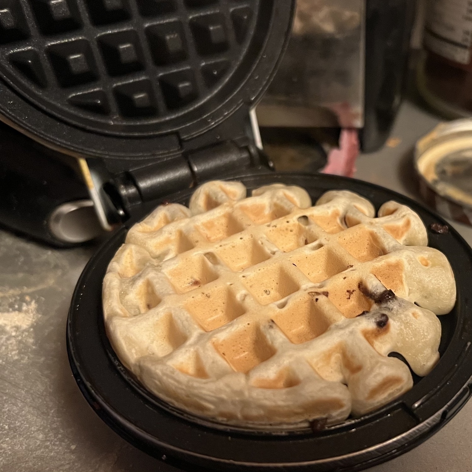 a small waffle iron is open, showing a small recently cooked golden colored waffle