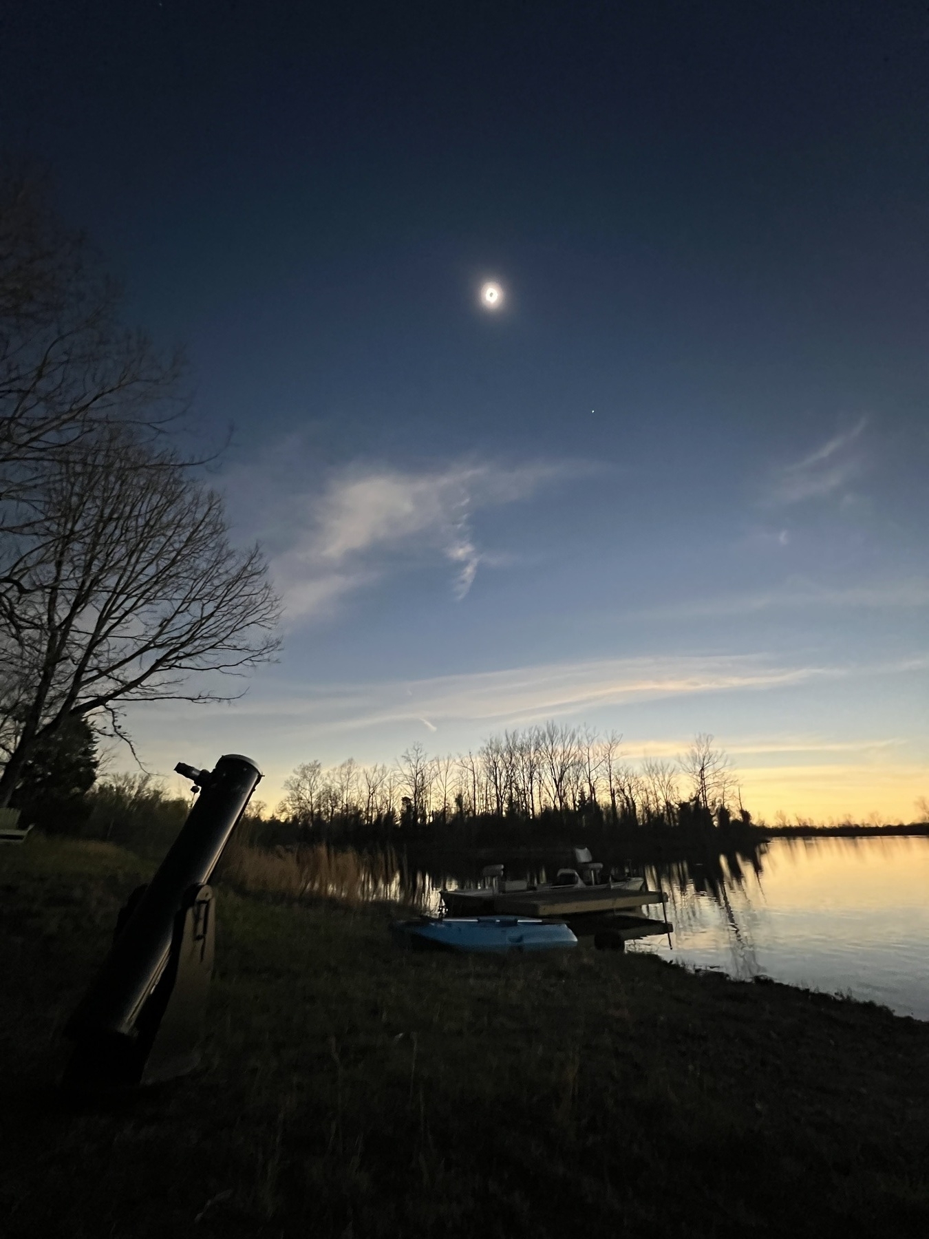 A telescope aimed at Sun in total eclipse with a lake