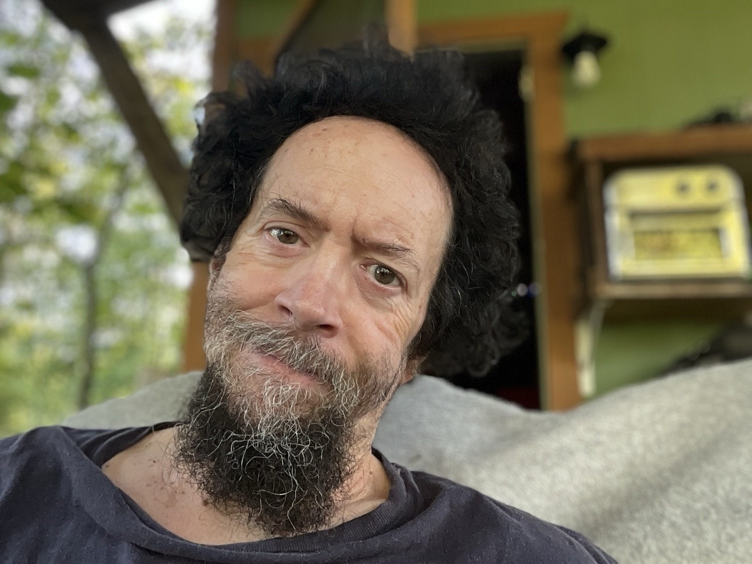 A fairly close-up portrait of a guy with a large forehead looking at the camera. His hair is black, his beard is streaked with gray and his eyes are not symmetrical.