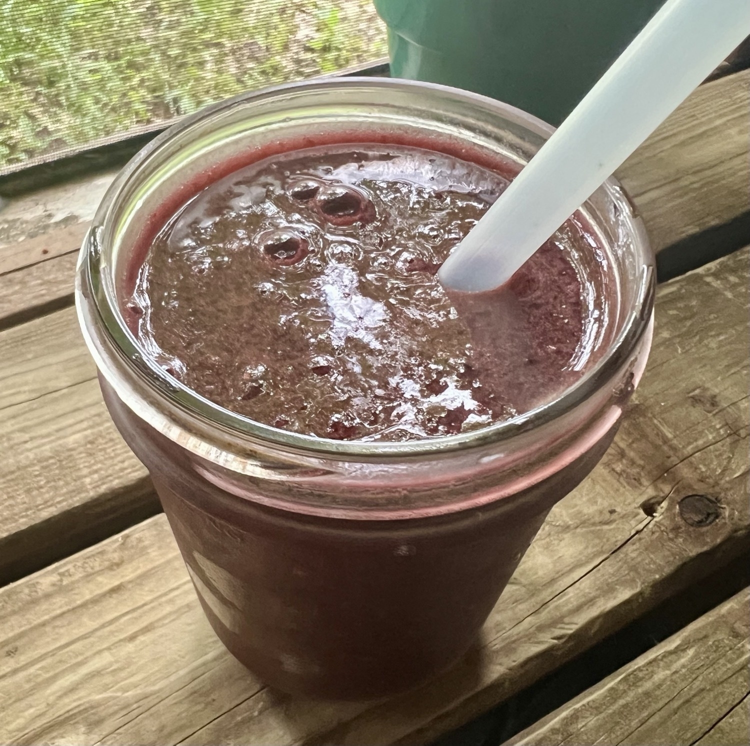 A mason jar of dark purple blackberry smoothie with a straw.