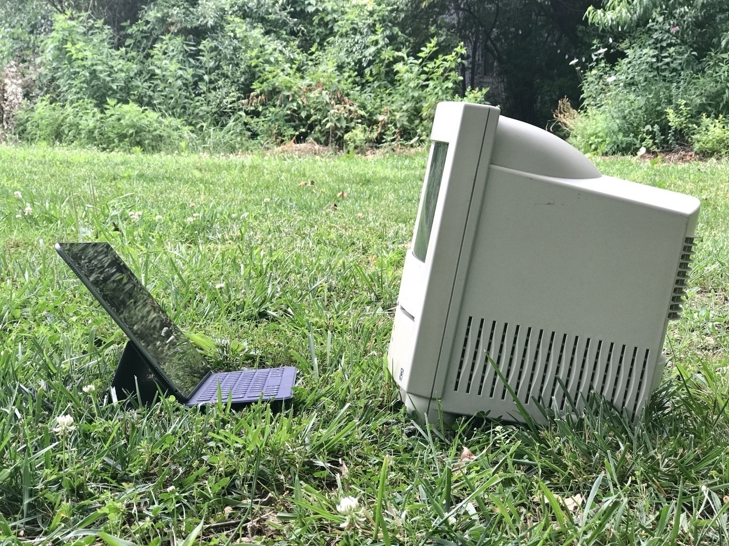 An iPad in a Keyboard Folio sits in the grass facing a Mac Color Classic