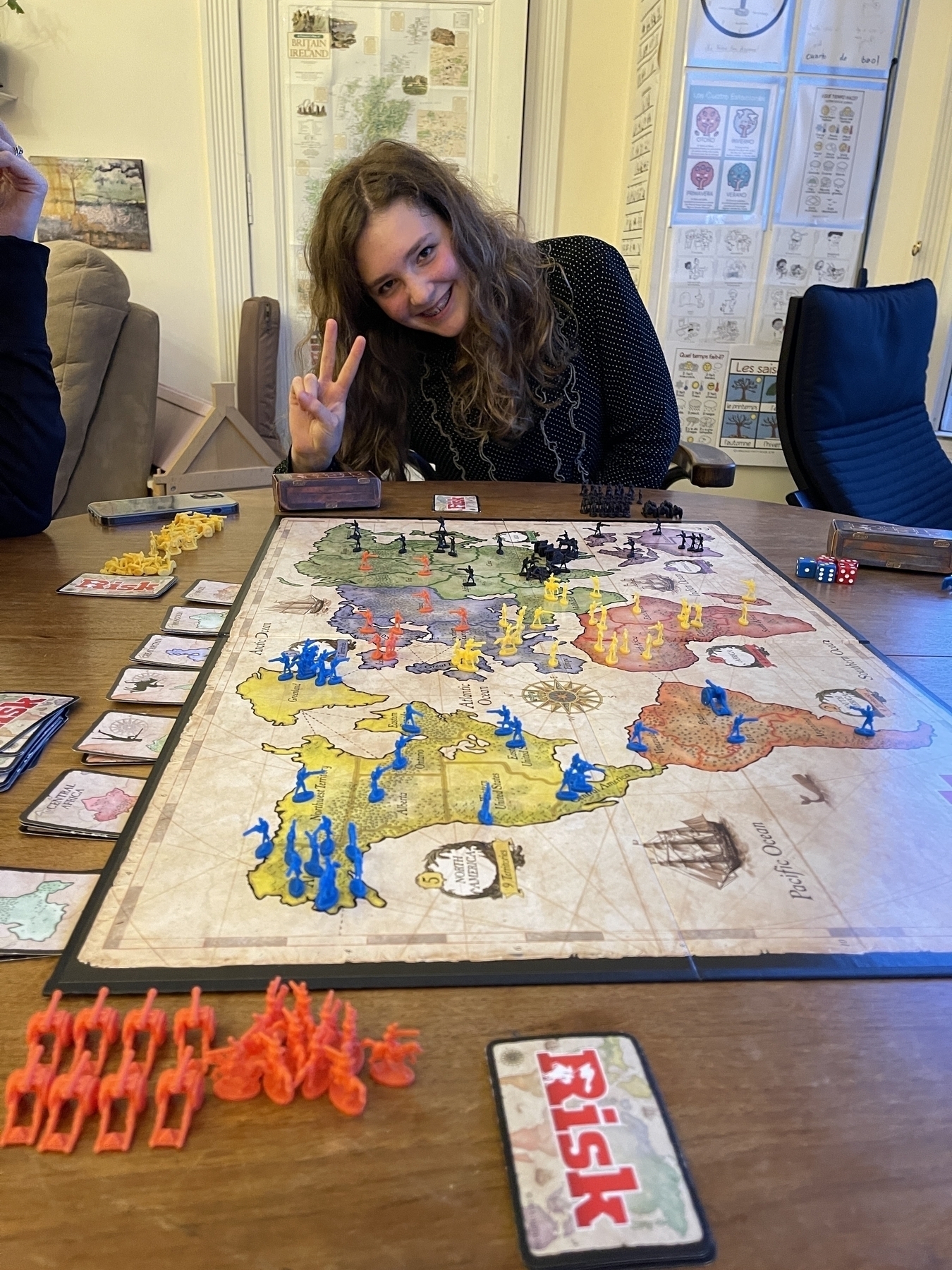 My orange armies surrounded on a risk board, with my ruthless oppressor/daughter making a peace sign in the background.