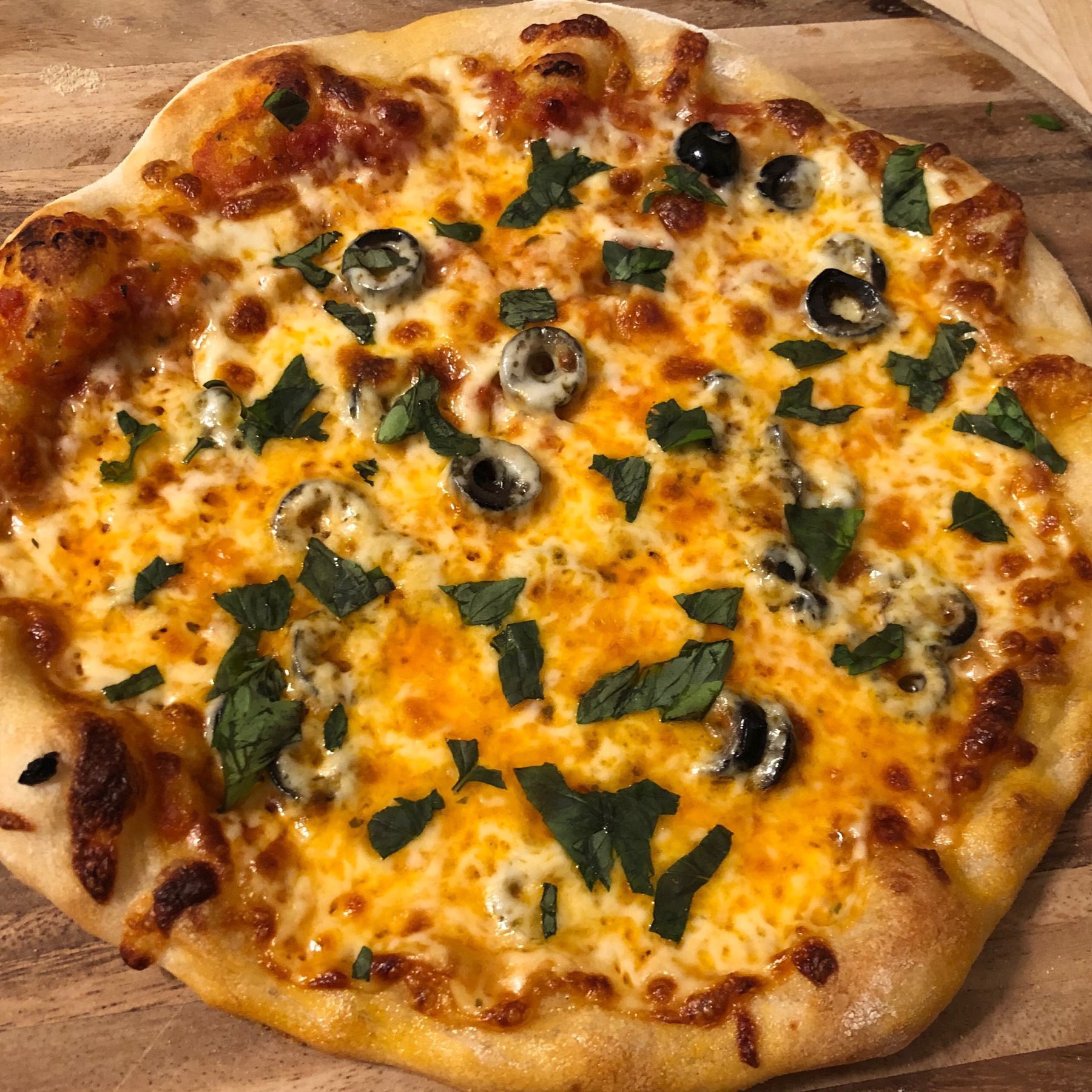 Fully baked pizza with olives and basil.