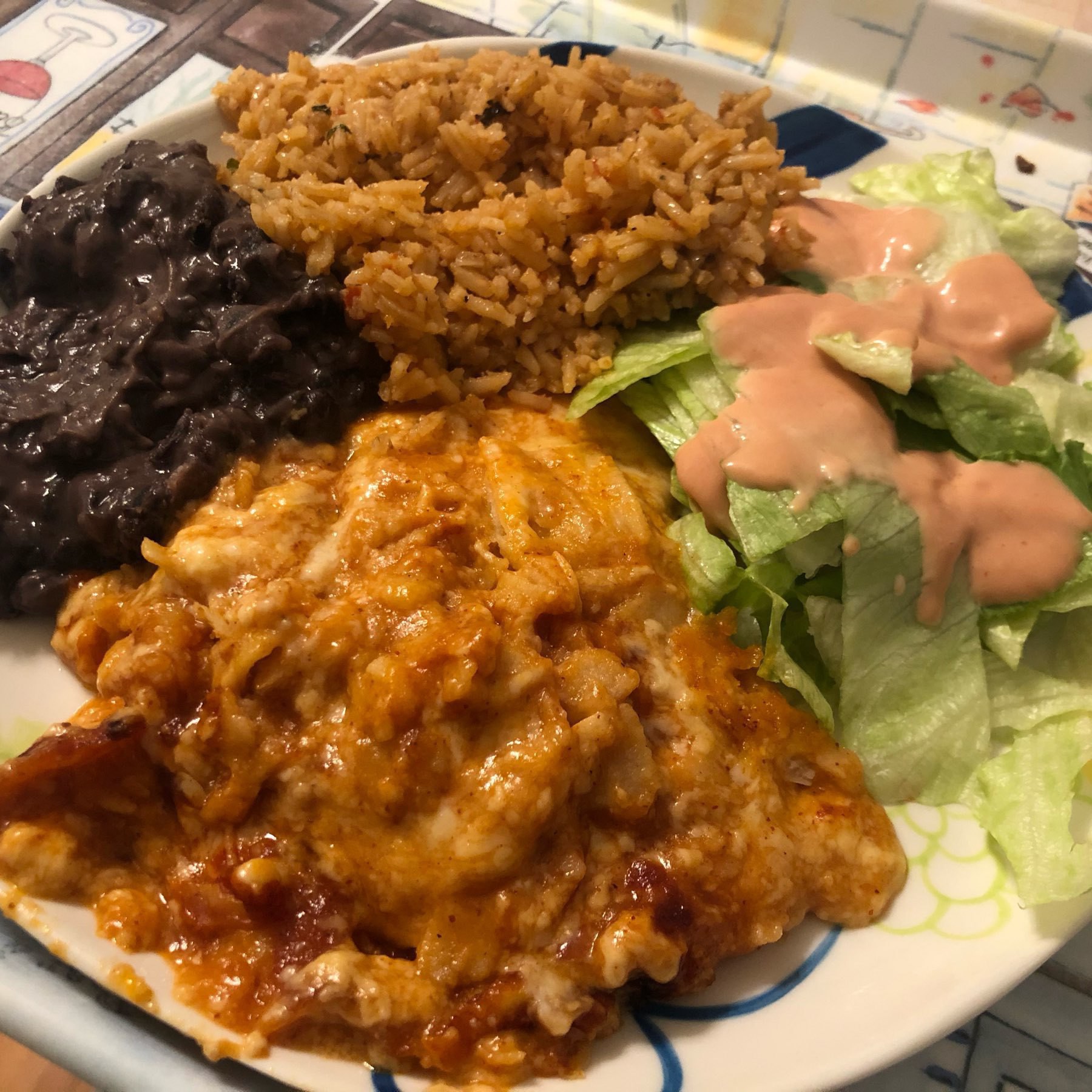 Picture of a plate with enchiladas, black beans, rice and a salad with thousand island dressing.