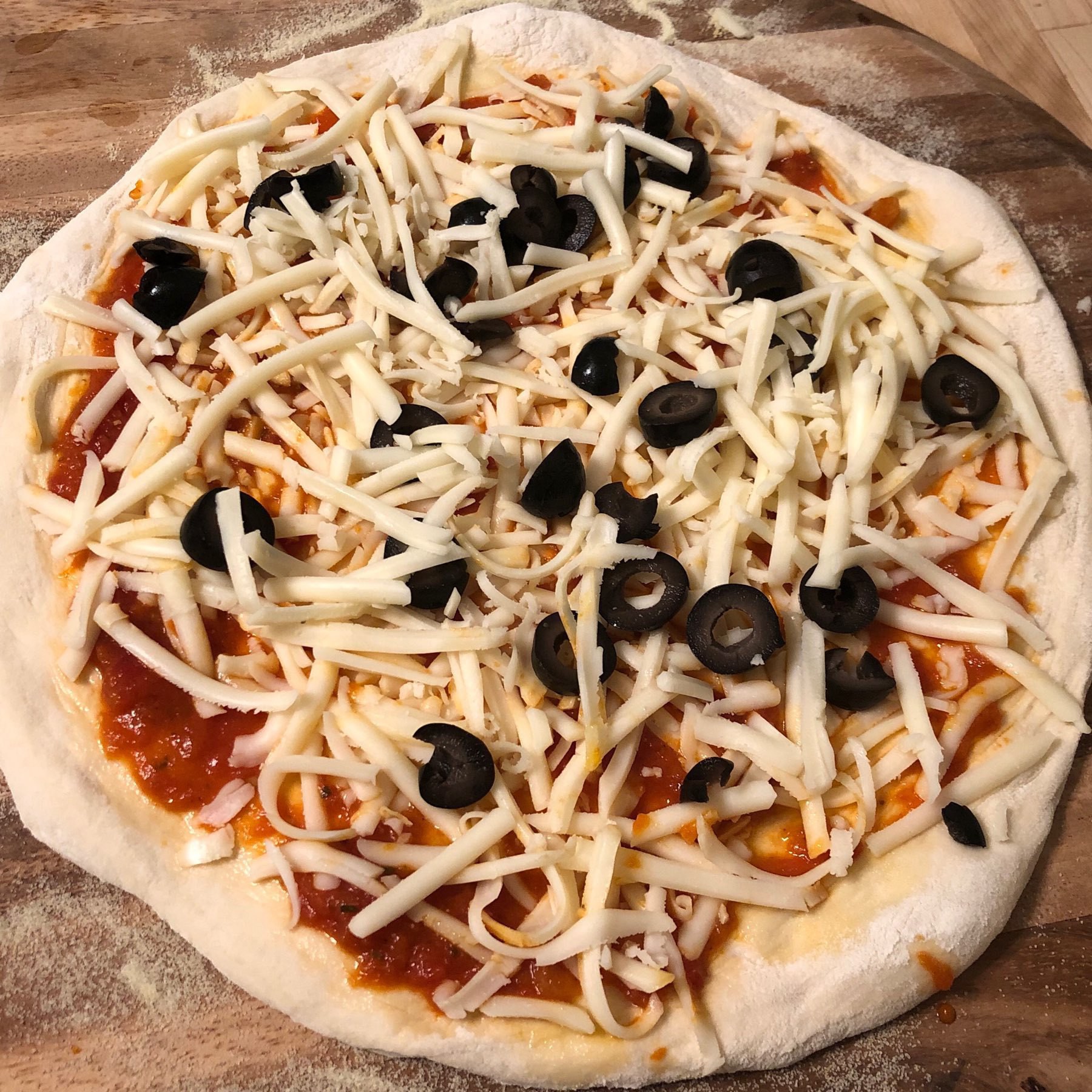 Raw pizza with grated mozzarella and black olives.