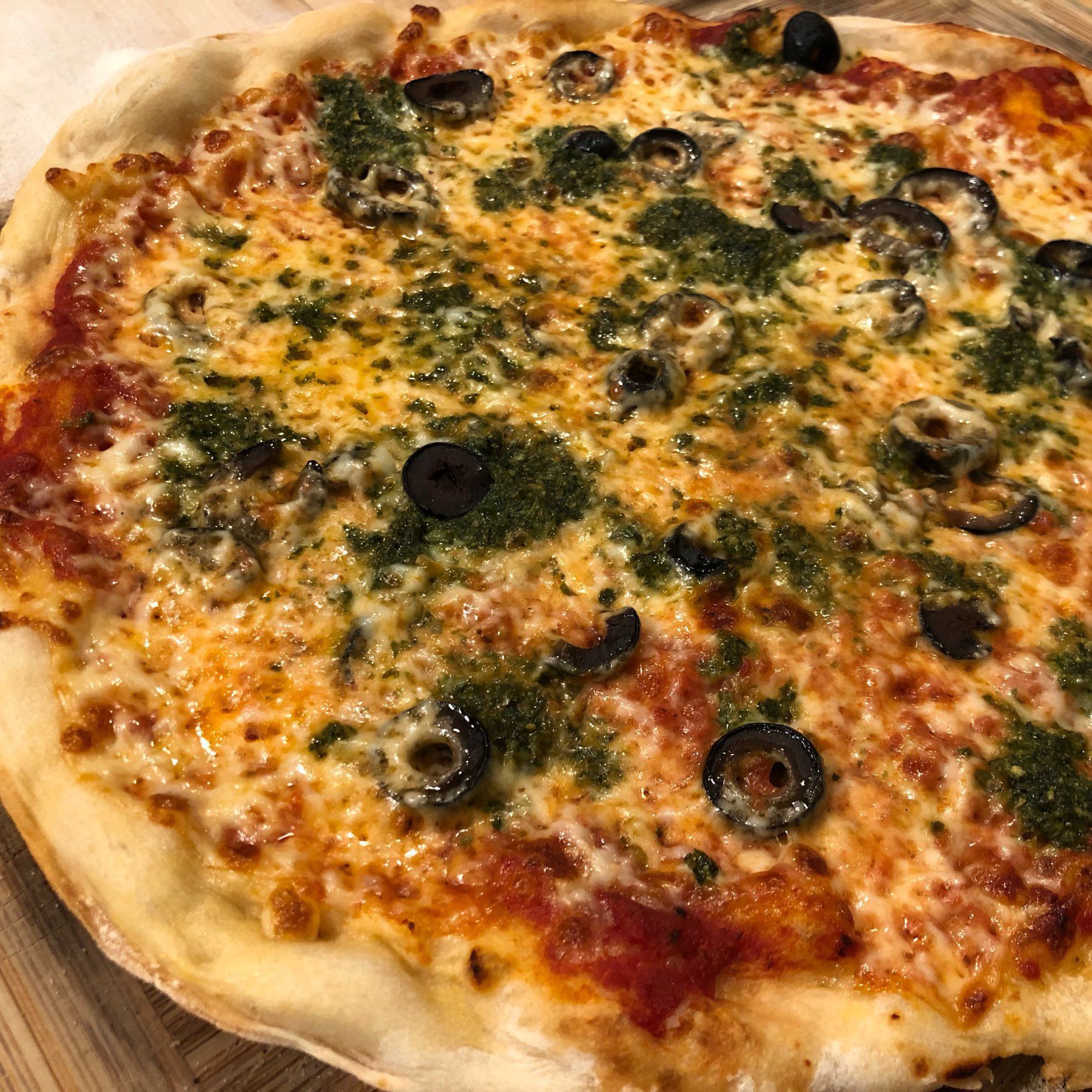 Close-up of a pizza with red sauce, cheese, black olives and pesto.