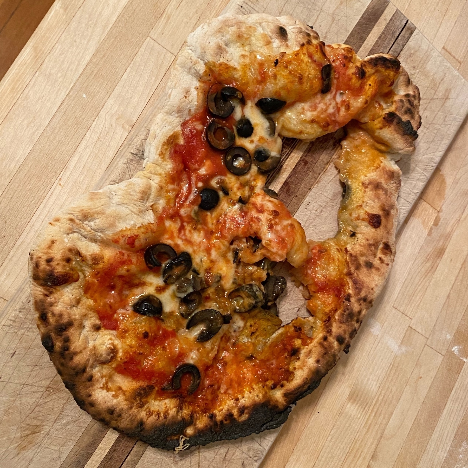 cheese and olive pizza in a non-circular shape with holes in it