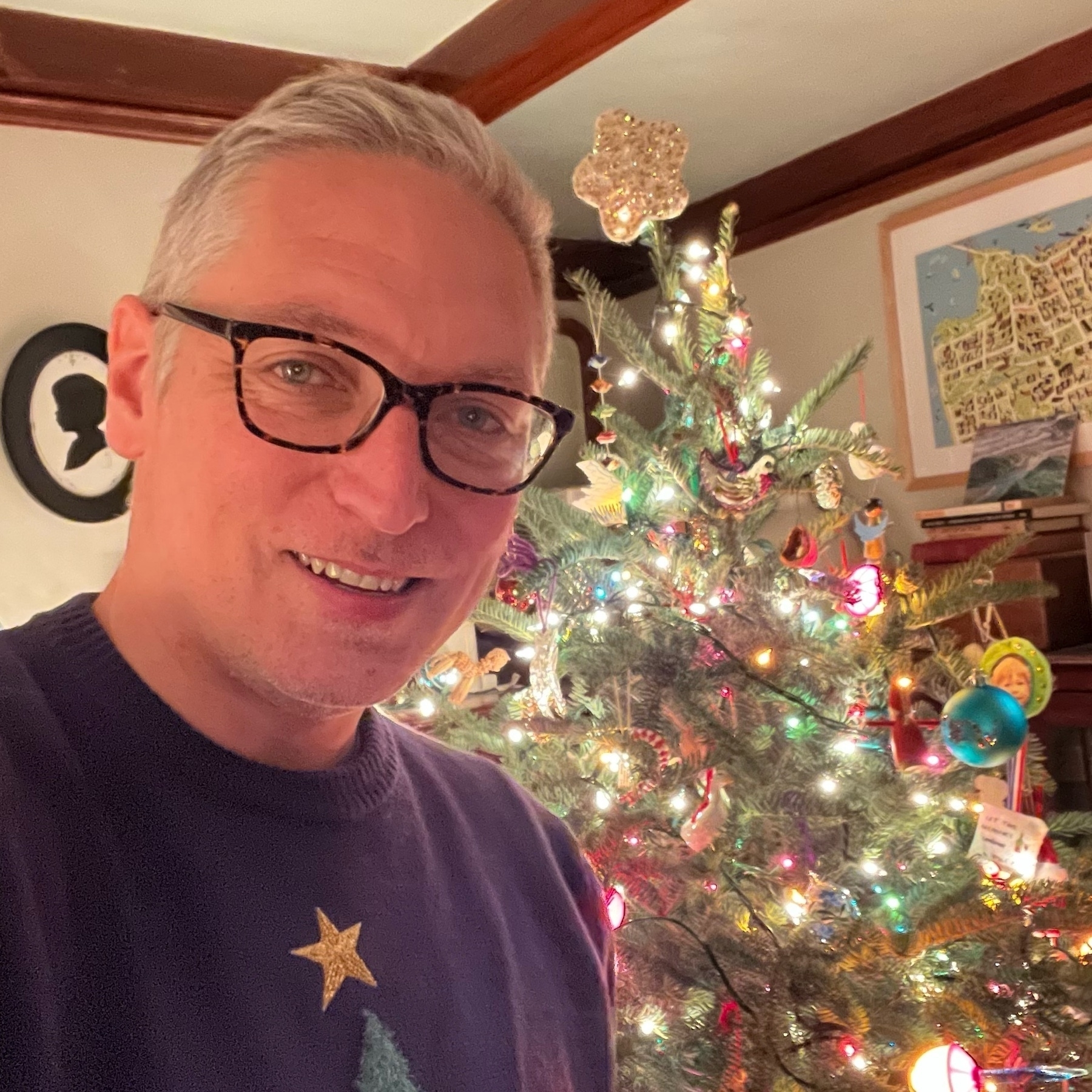 selfie wearing a christmas tree sweater with a star on top, next to a real lit christmas tree in our living room