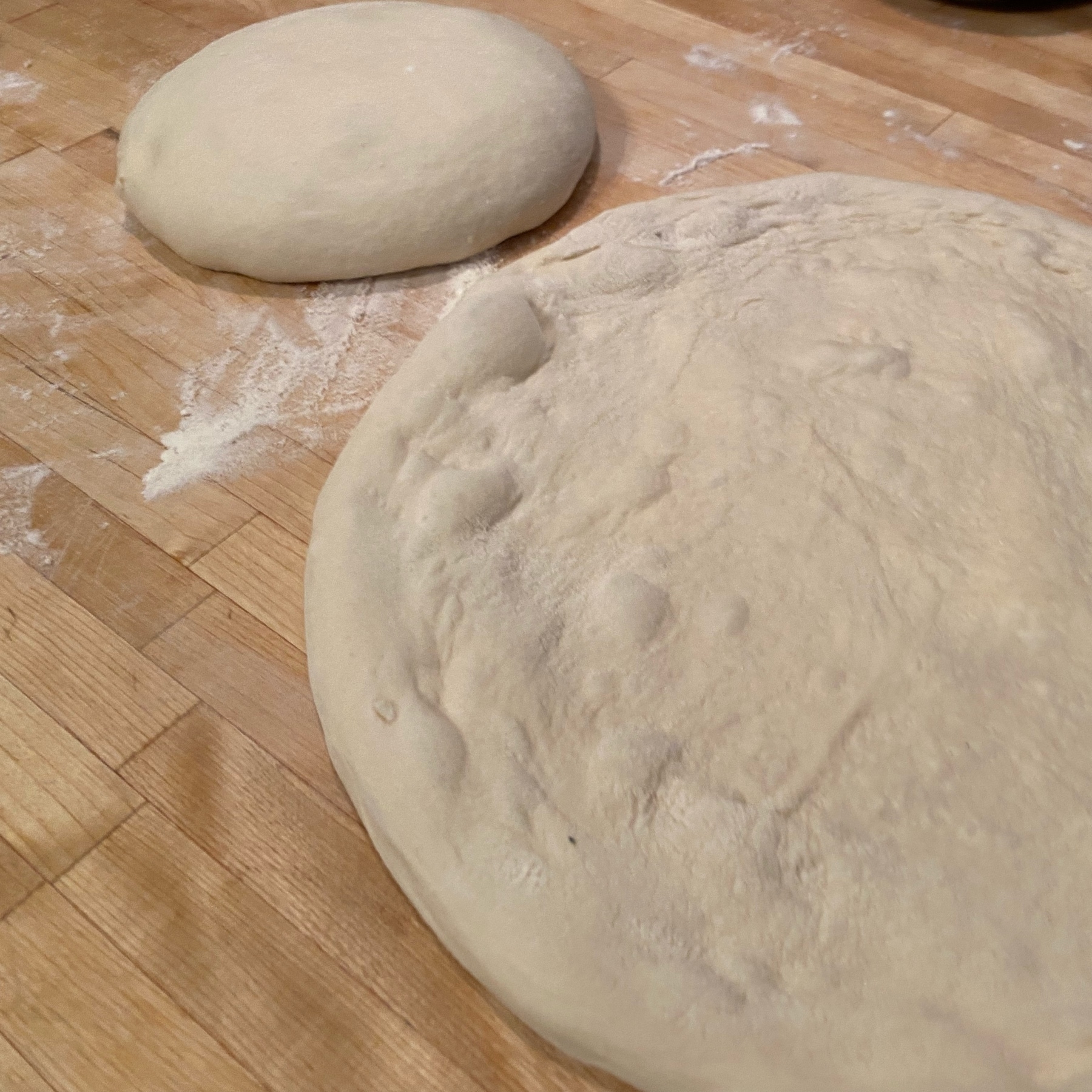 two dough balls, one stretched into a pizza shape and one in a round mound