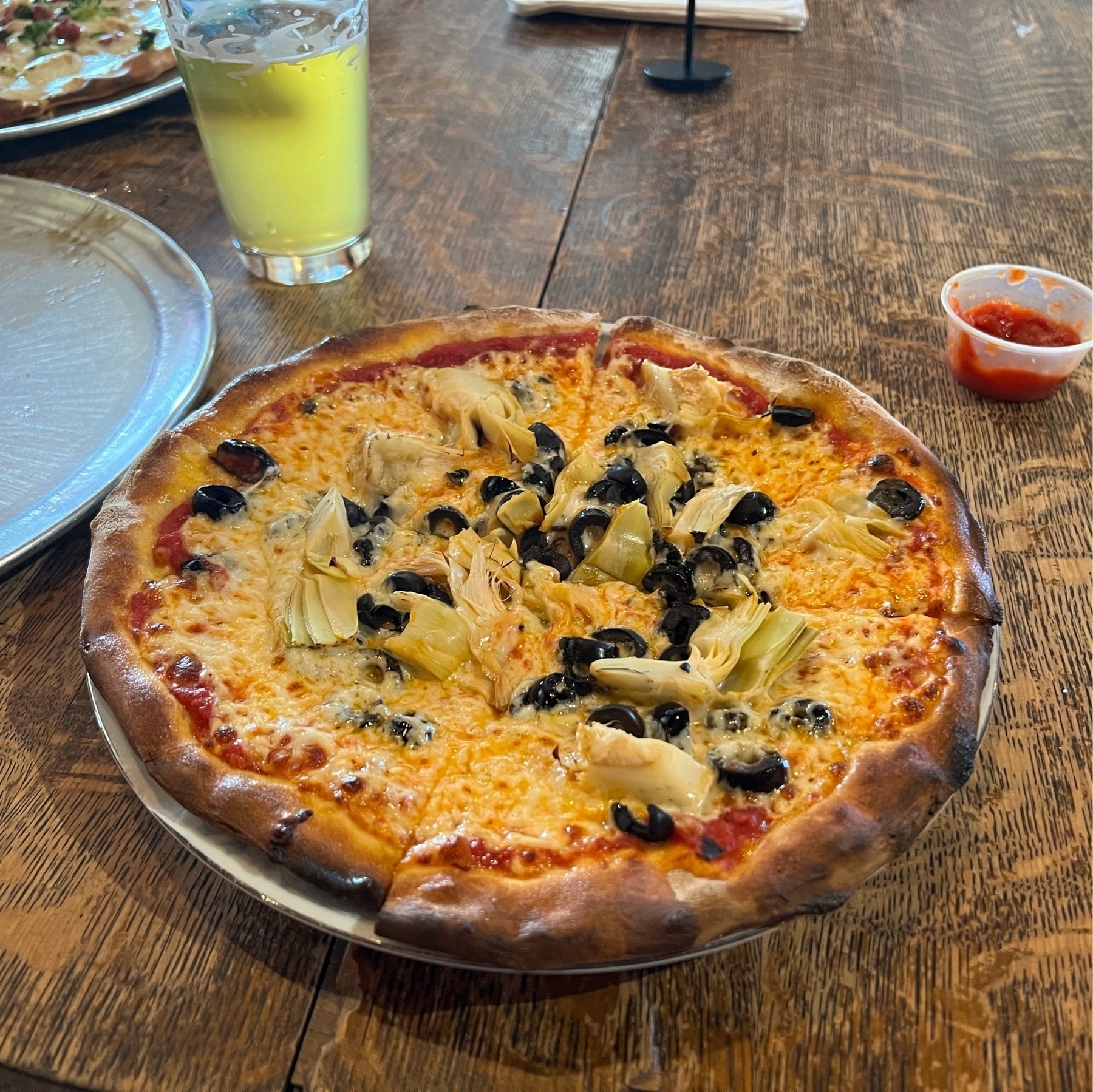 Personal-sized olive and artichoke heart pizza with a pint of beer