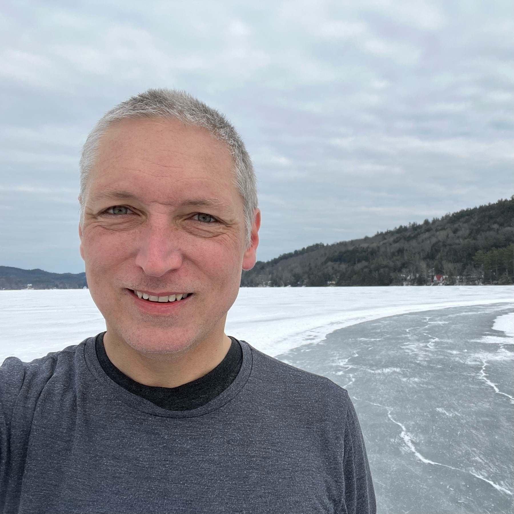 selfie in black thermal shirt against snowy backdrop with cleared "river" of skating ice