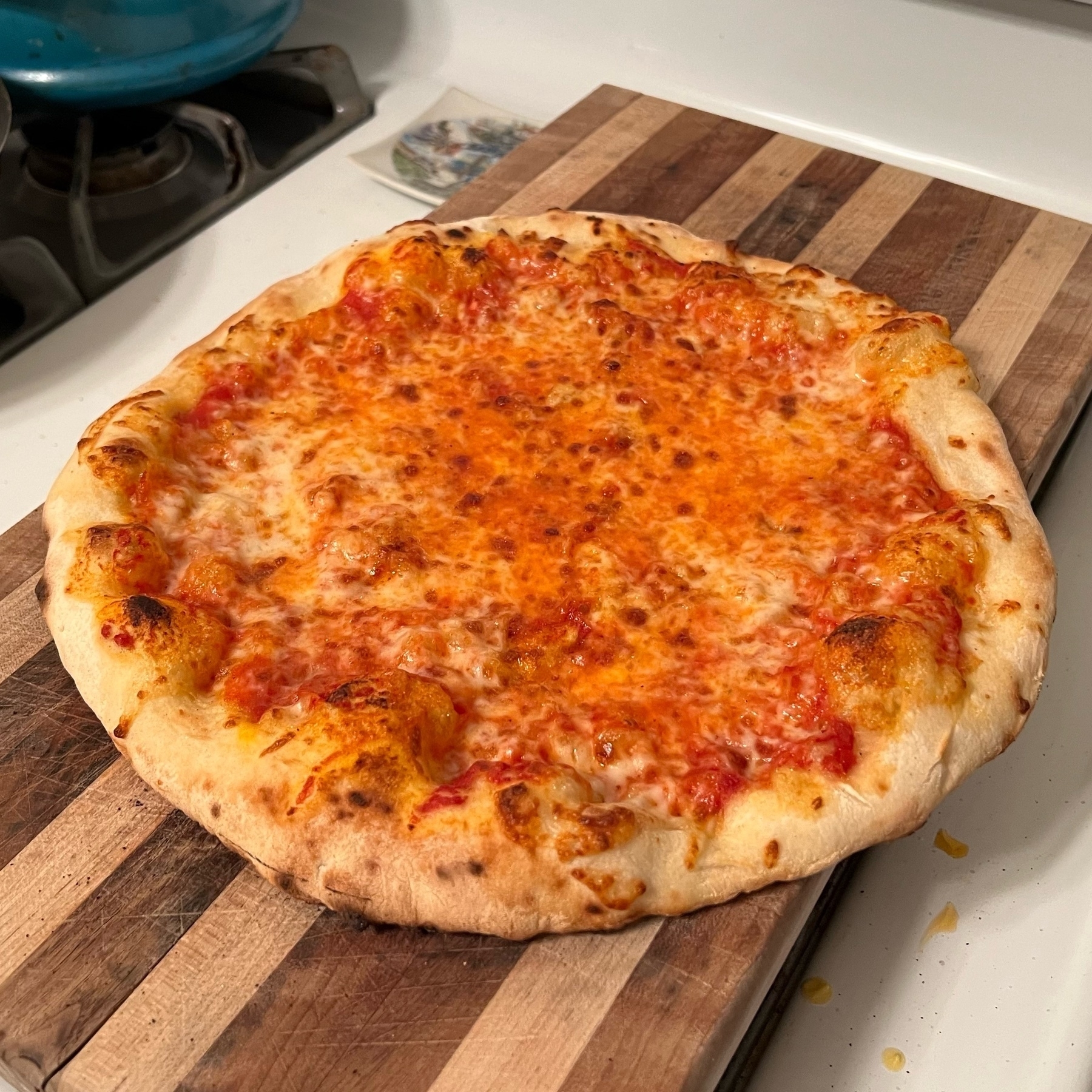 medium sized homemade cheese pizza with puffy crust, sitting on a wooden cutting board on a kitchen stove
