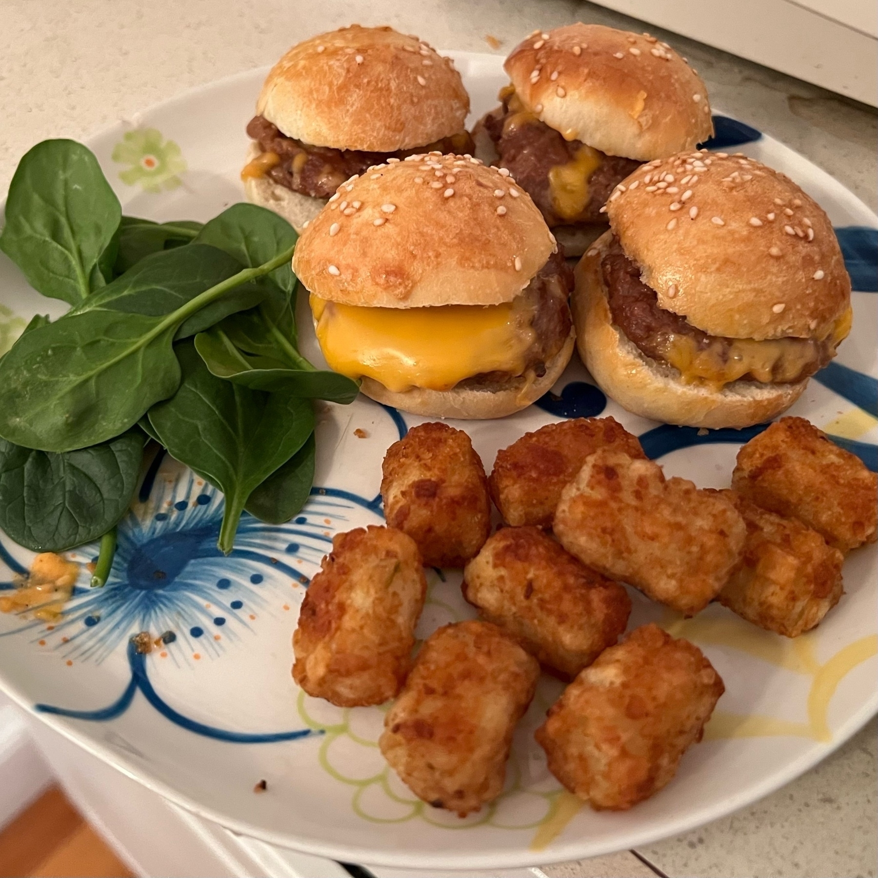 picture of a dinner plate with spinach, tater tots, and four tiny cheeseburgers