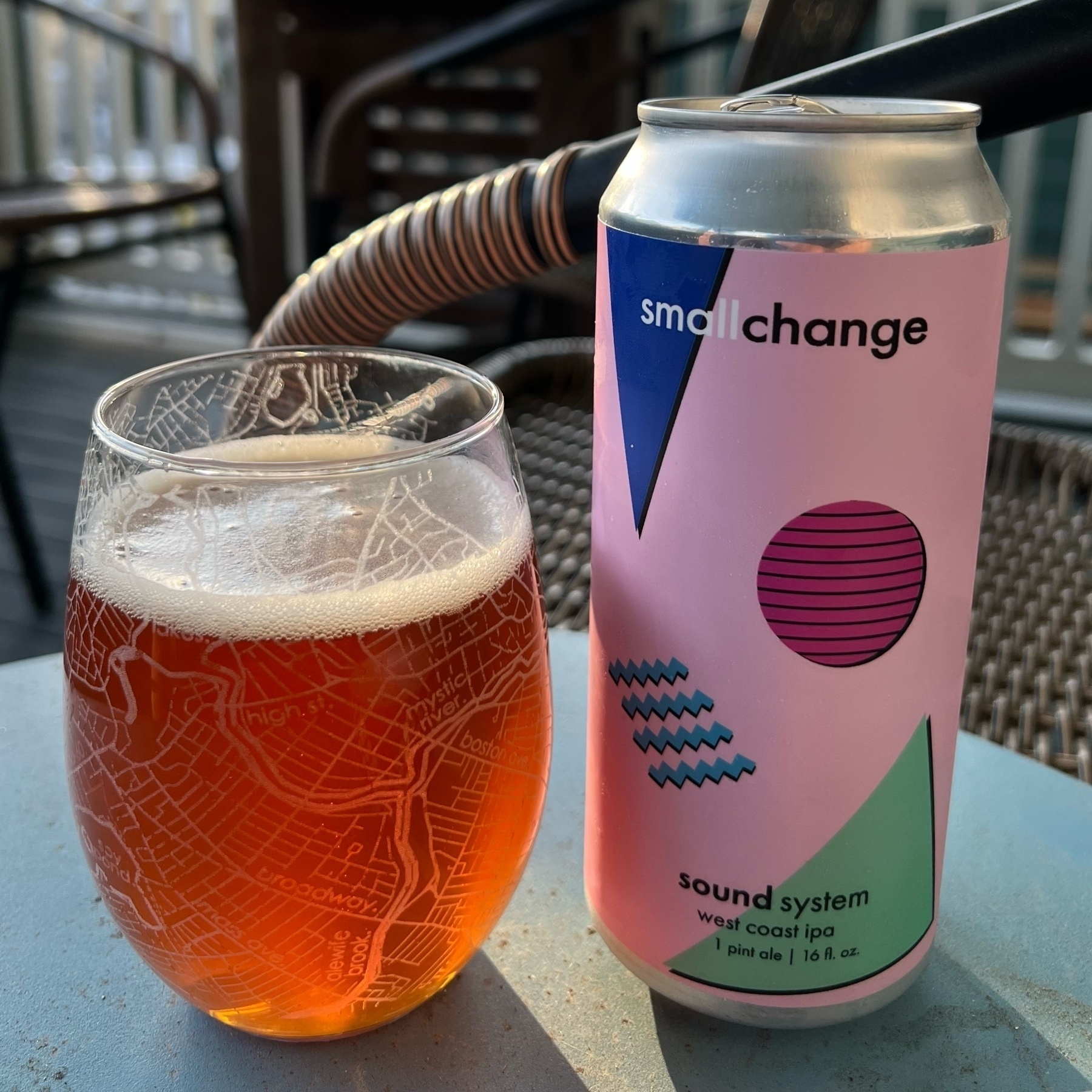 a stemless glass filled with light amber beer, next to a pink beer can labeled "small change - sound system - west coast ipa"