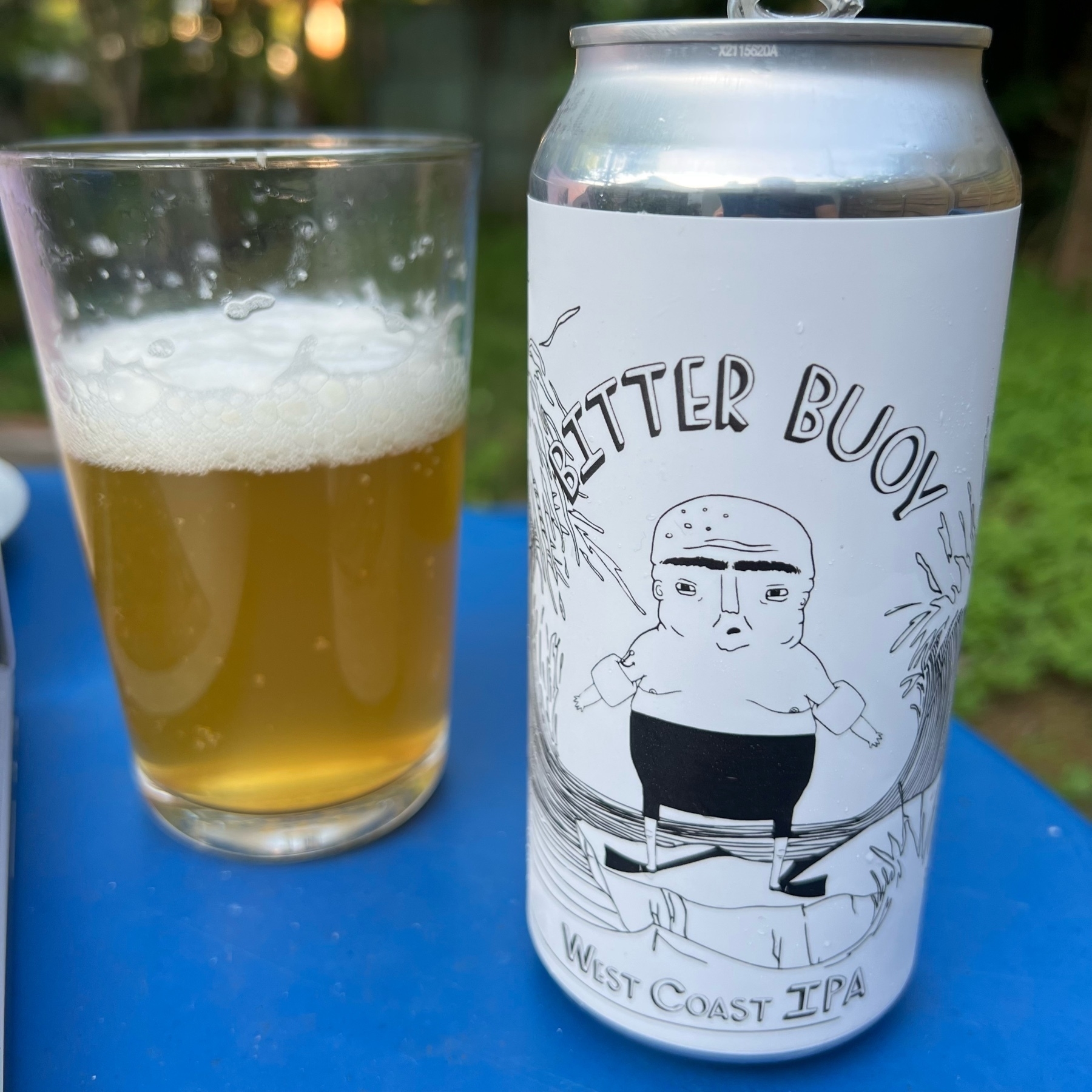 A pint glass half full of golden ale and a beer can with a monochrome design of a cartoon man with swimming floaties and the title “Bitter Buoy”