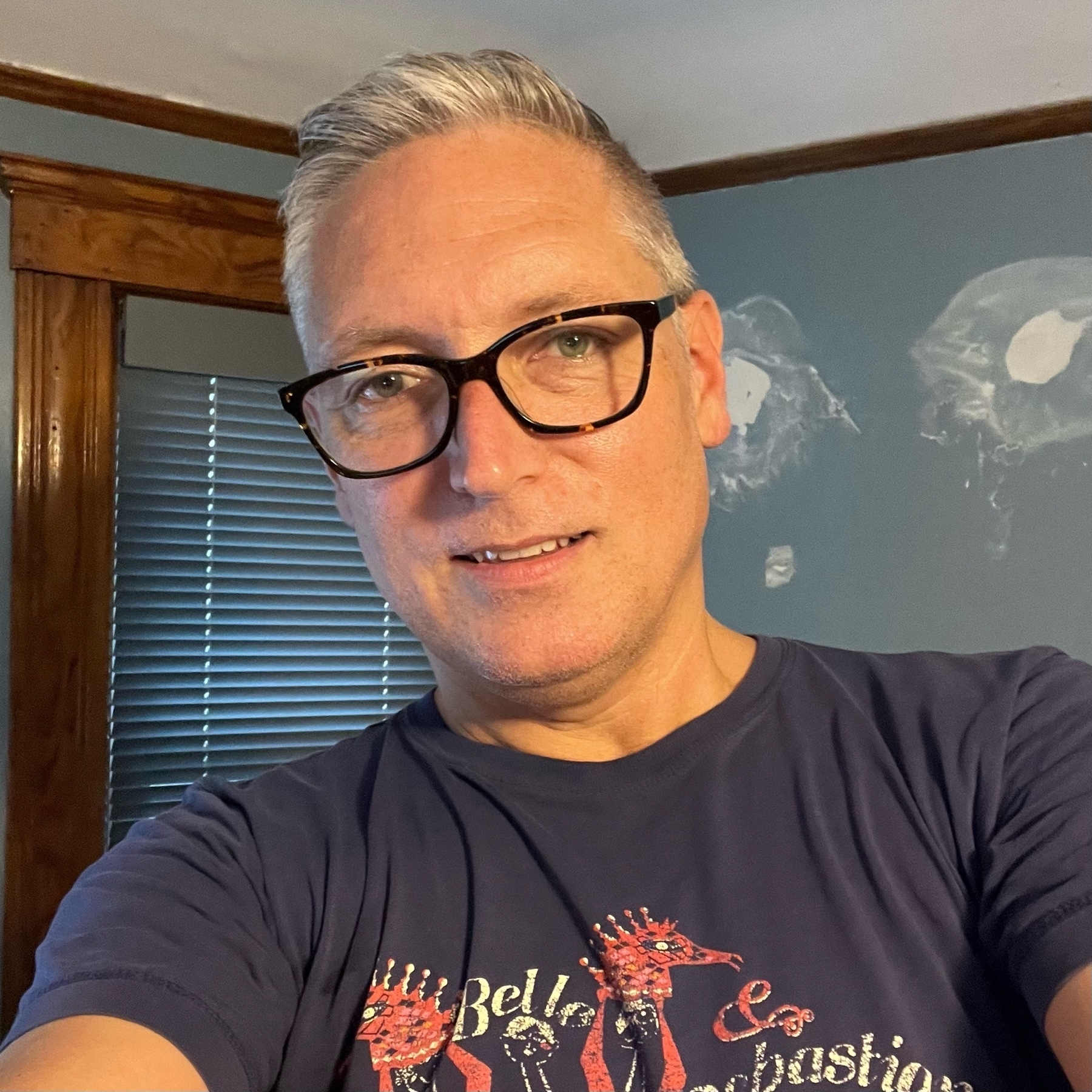 selfie of a caucasian man with grey hair wearing glasses, wearing a Belle @ Sebastian t-shirt