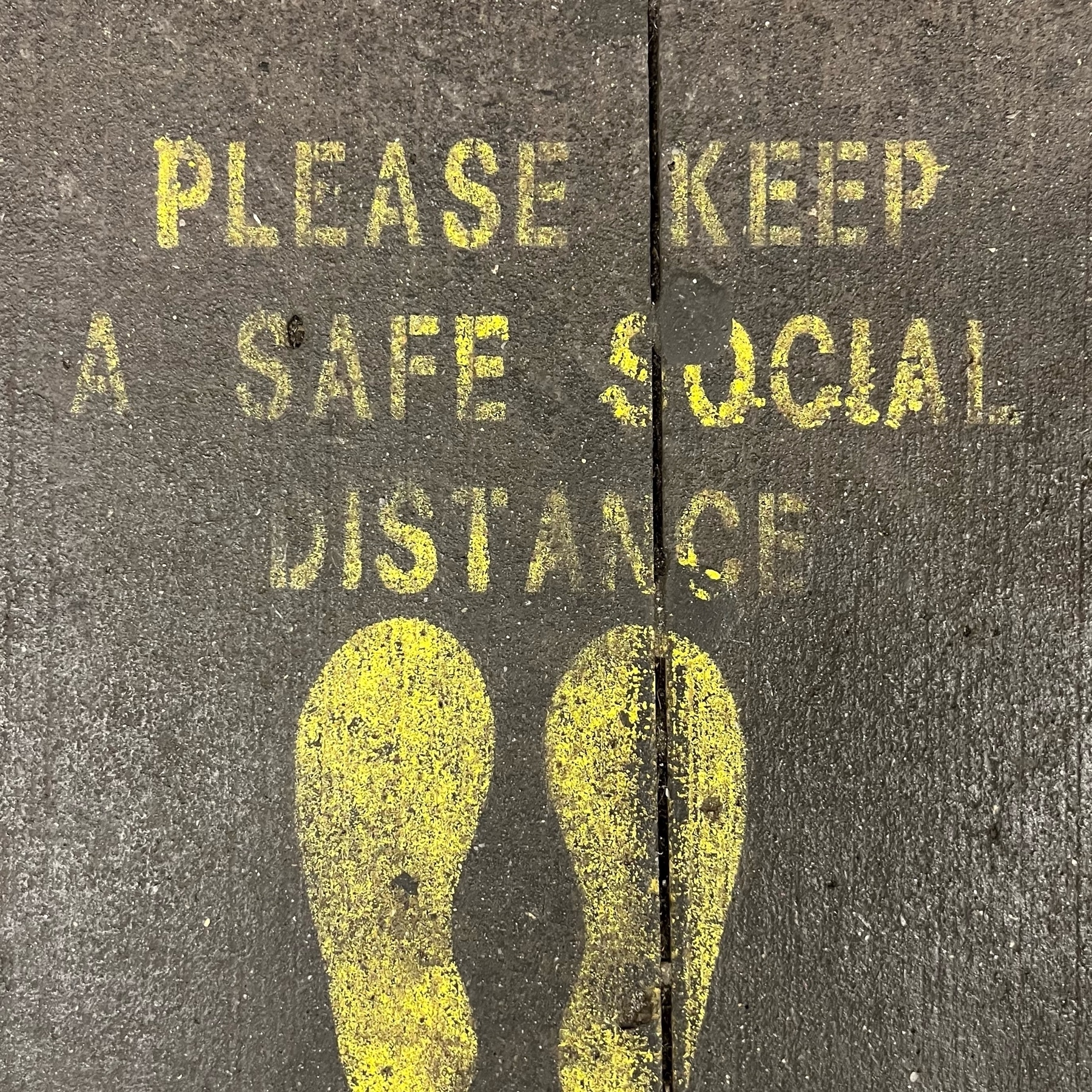 stencil painted on subway platform with feet outline and text "please keep a safe social distance"
