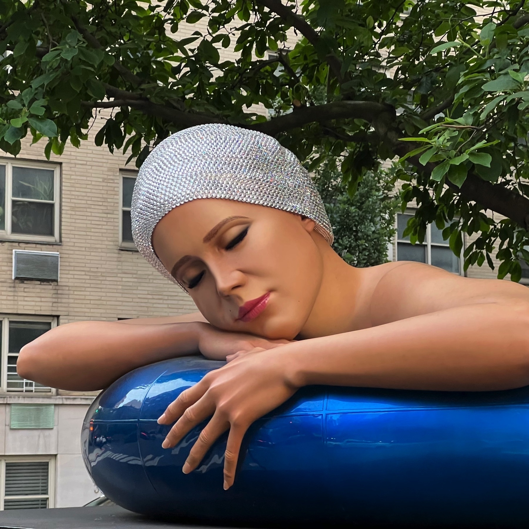 Larger than life realistic sculpture of a woman in a swimcap, resting on an inner tube.