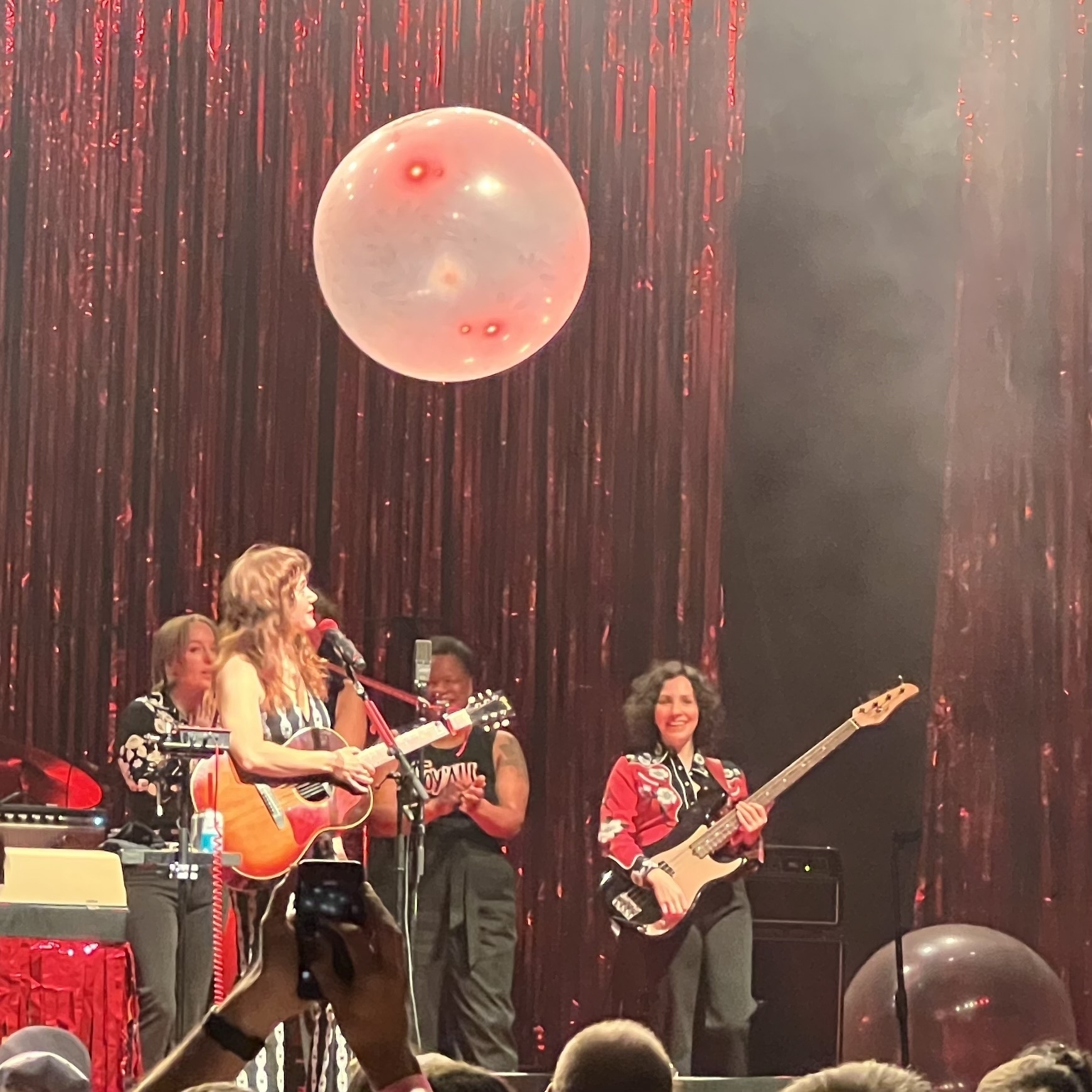 Jenny Lewis and bandmates on stage, laughing, under a suspended balloon.