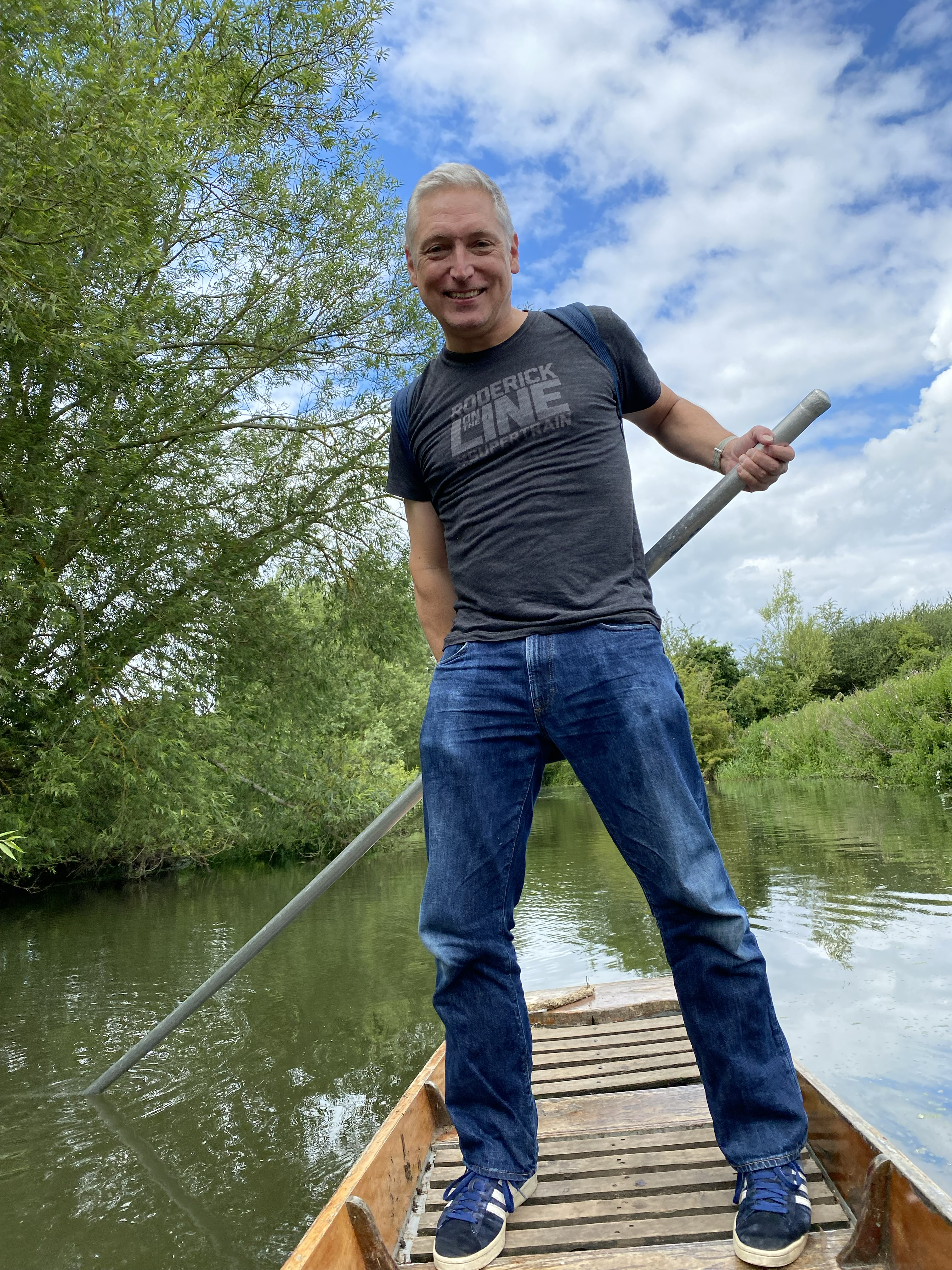 Picture of Daniel standing at the back of a British punting boat, long pole behind his back, standing akimbo. He’s wearing a “Roderick on the Line” t-shirt, surrounded by Oxford’s Cherwell river and greenery around.