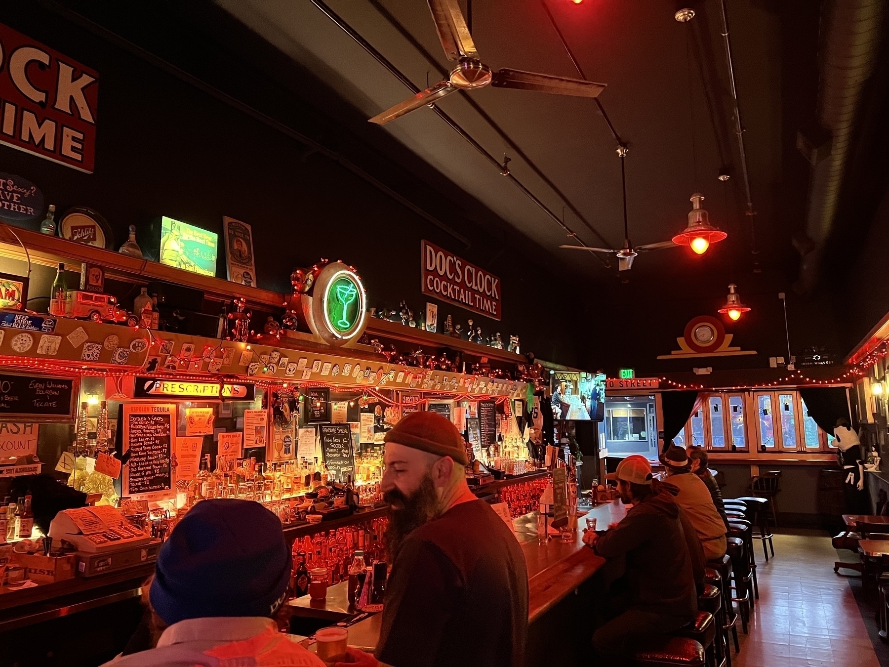 Photo of a bar with red tones and lots of red light. A sign on the wall reads “Doc’s Clock Cocktail Time”