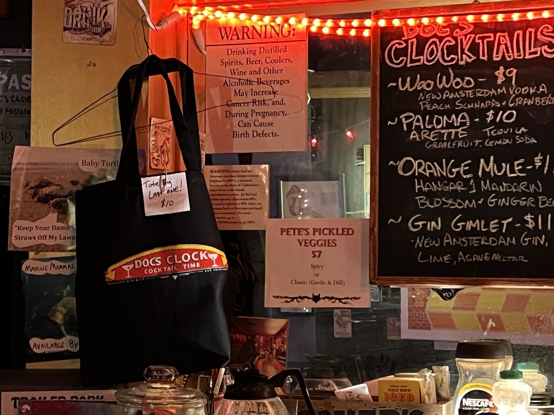 Wall of a bar with drink menu and a tote bag for sale with label “Doc’s Clock”. A tag on the bag says “Last One - $10”. 