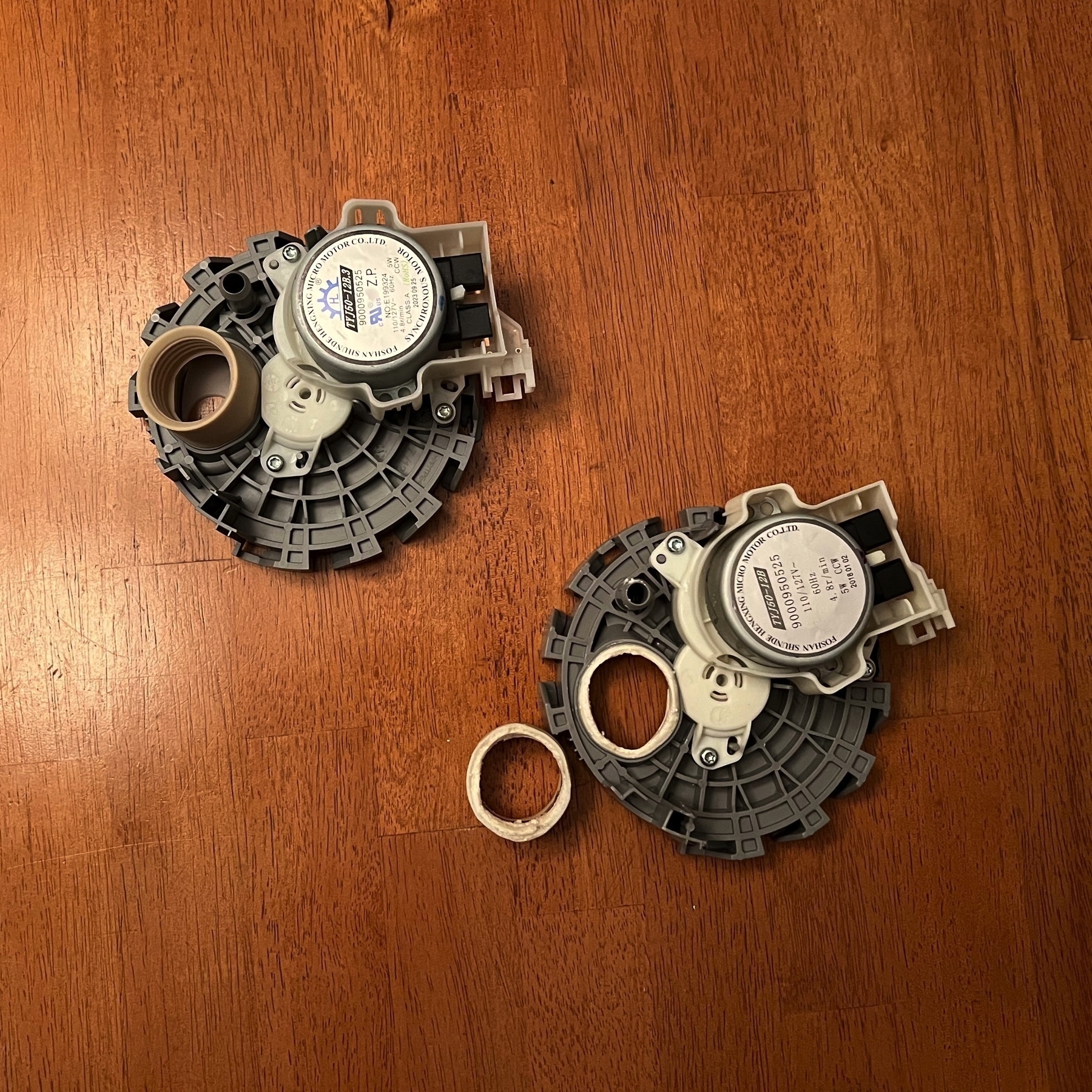 Two dishwasher diverter valves, which are circular plastic gizmos with a rubber tube insert, and an attached motor. The valve on the left is brand new and everything is in tact. The valve on the right has a visibly detached and broken rubber tube.