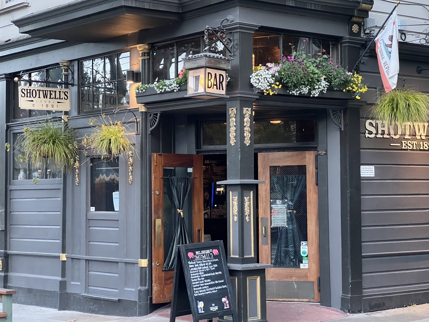 Exterior view of Shotwell’s bar in San Francisco. A corner building with flowers and plants adorning the entrance