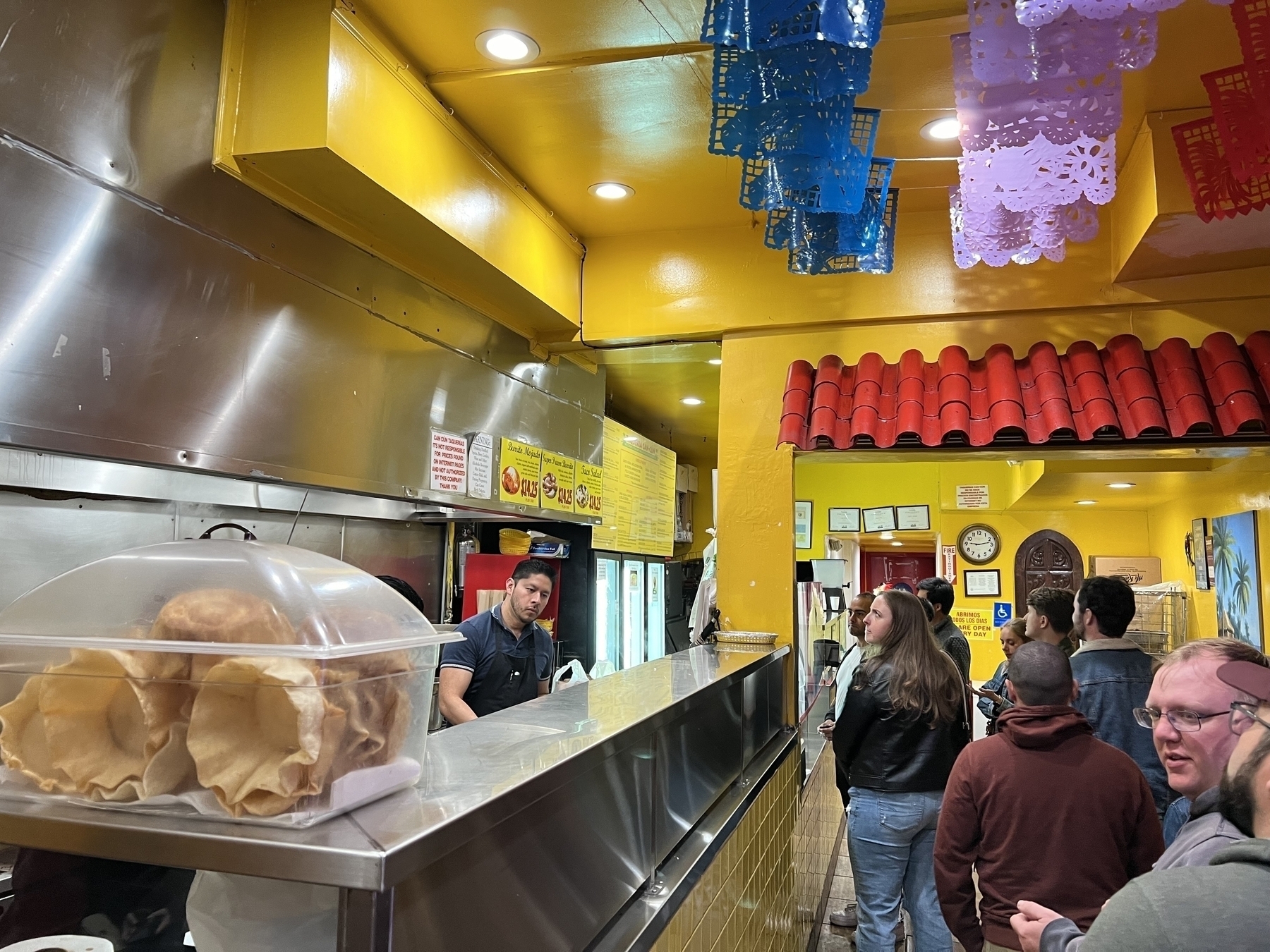 A taqueria counter with people standing in line to order.