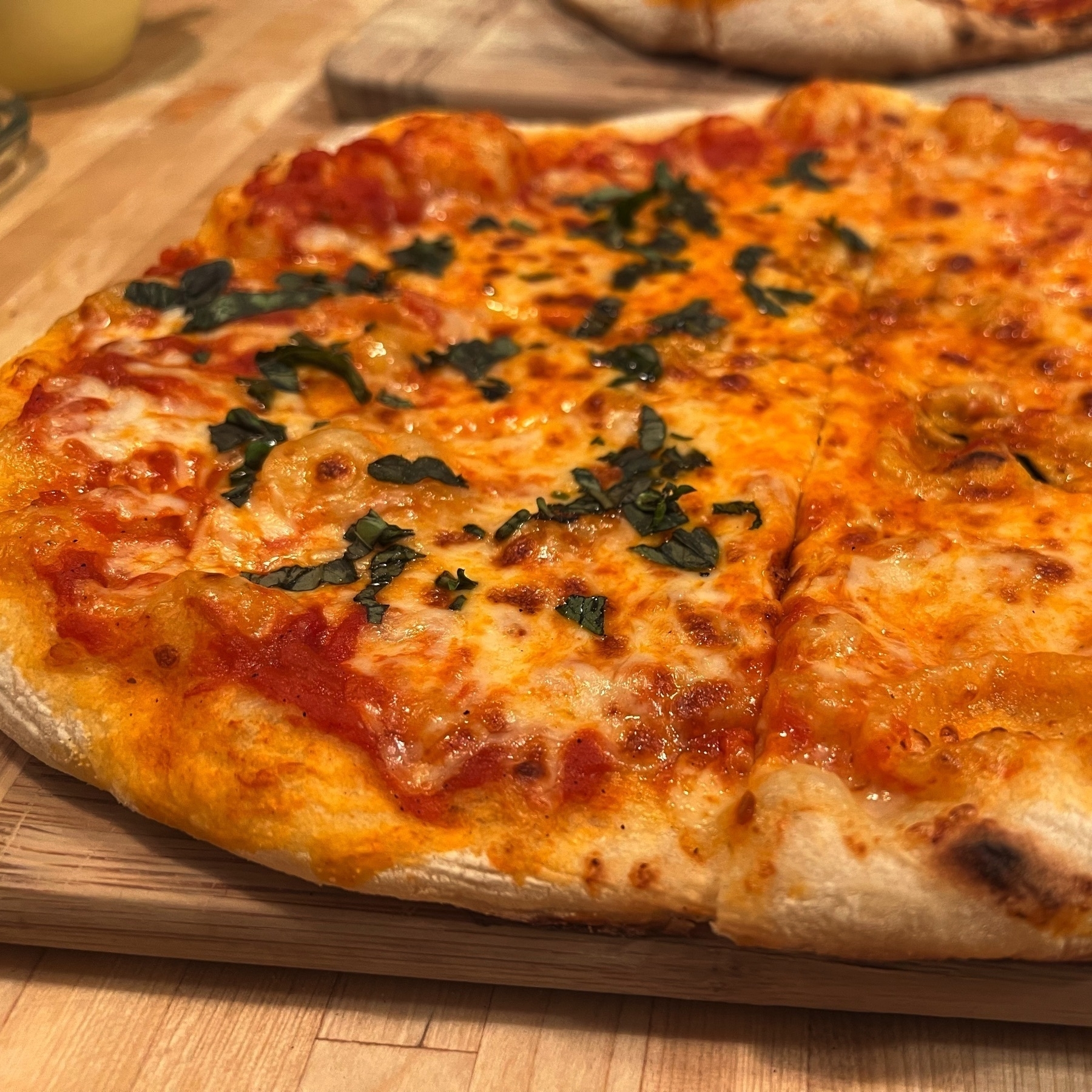 Close-up picture of a glistening cheese pizza, sliced in half, with basil shreds covering one half of the pie.