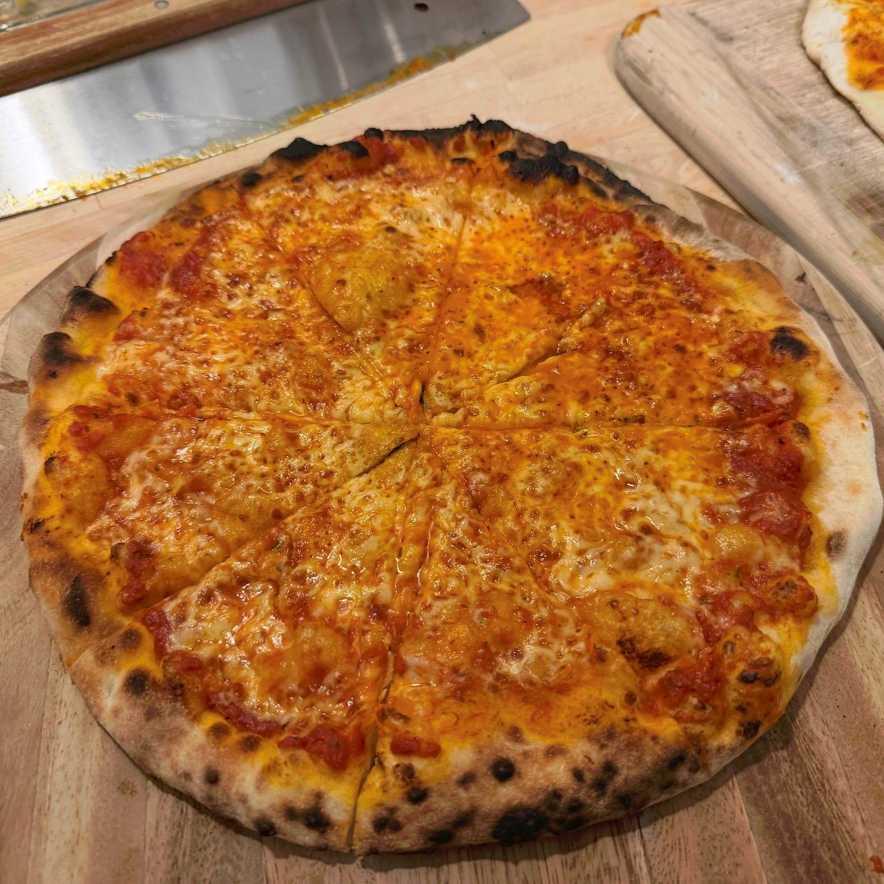 A cooked pizza with charred edges, bubbles, and a red/orange splotched appearance where the cheese and sauce have melted together.