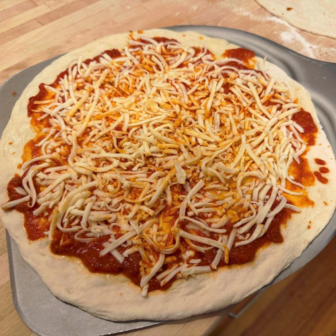 An uncooked homemade pizza with red sauce spilling out the edges under grated cheese that has turned partially red from mixing with the sauce.
