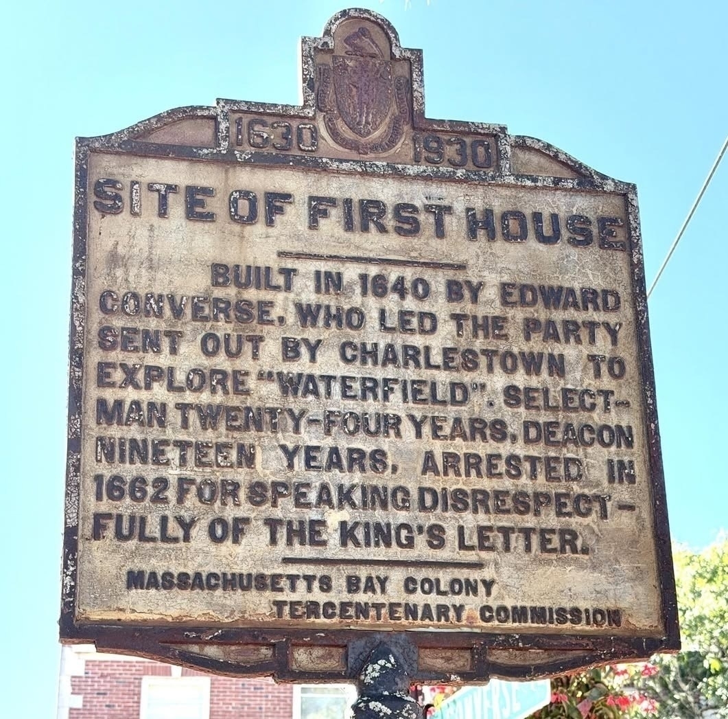 Picture of a historic plaque erected in 1930 to commemorate 300 years of the Massachusetts Bay Colony’s independence from Britain. The plaque reads: “SITE OF FIRST HOUSE. BUILT IN 1640 BY EDWARD CONVERSE, WHO LED THE PARTY SENT OUT BY CHARLESTOWN TO EXPLORE ‘WATERFIELD’. SELECTMAN TWENTY-FOUR YEARS, DEACON NINETEEN YEARS, ARRESTED IN&10;1662 FOR SPEAKING DISRESPECTFULLY OF THE KING'S LETTER.”