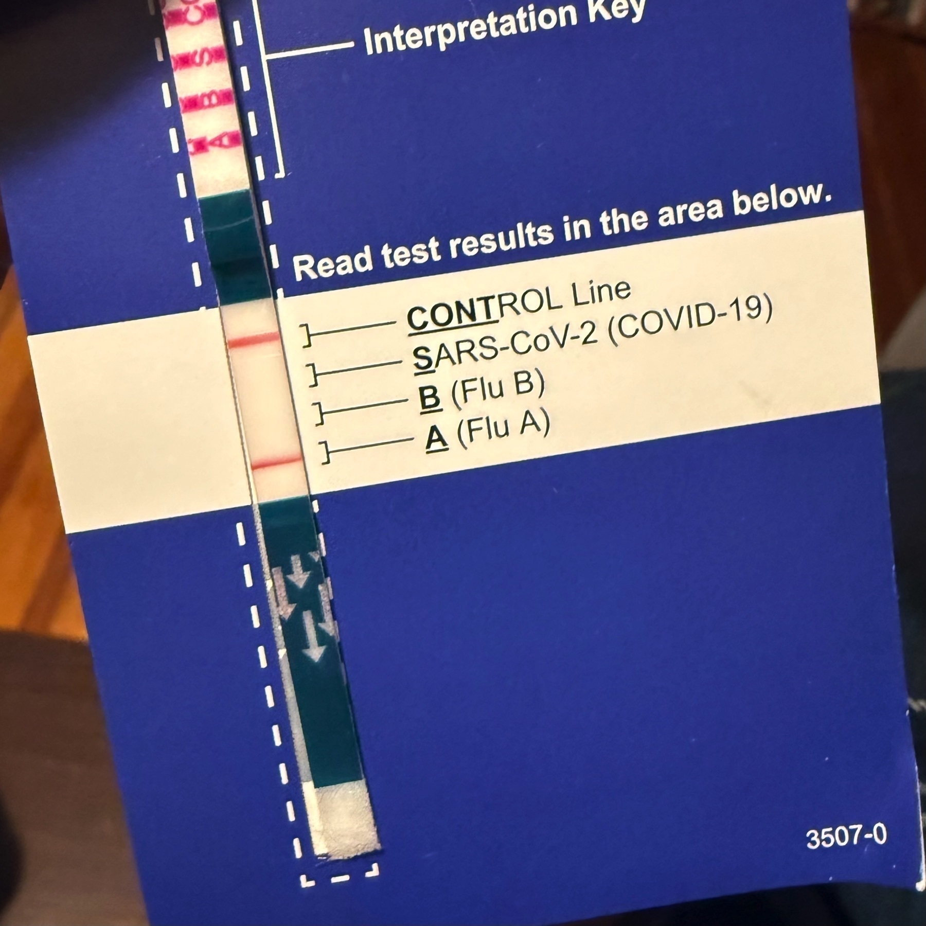 A Covid+Flu test strip held against an intrepretation key on paper, showing that the control line and “Flu A” lines were activated.